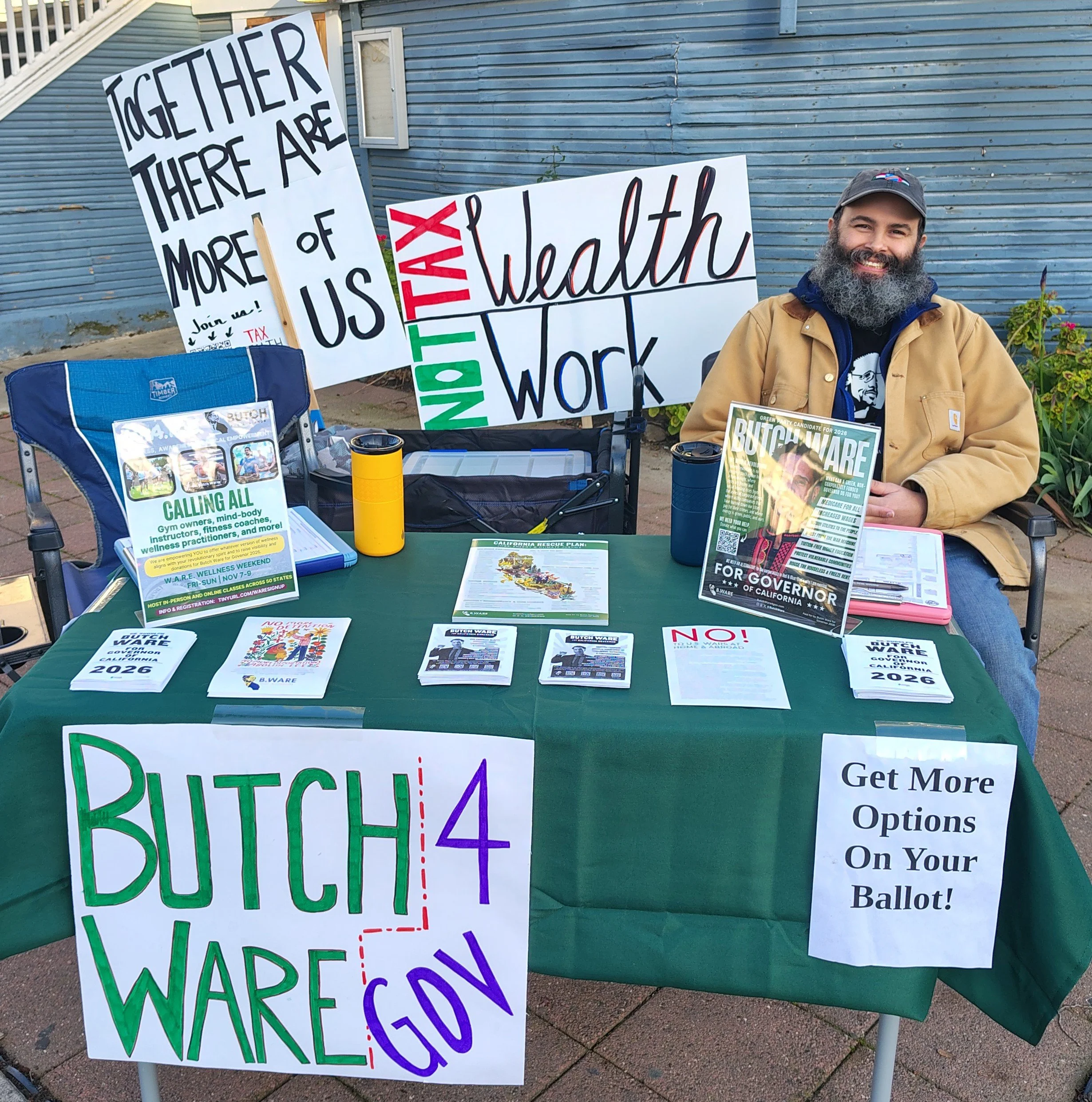 Various signs and flyers related to political campaigning for Ware, a candidate for governor in California in 2026. One sign emphasizes the importance of voting, and others call for voter participation, mentioning issues such as ballot options and voting procedures. The setup appears to be outdoors.