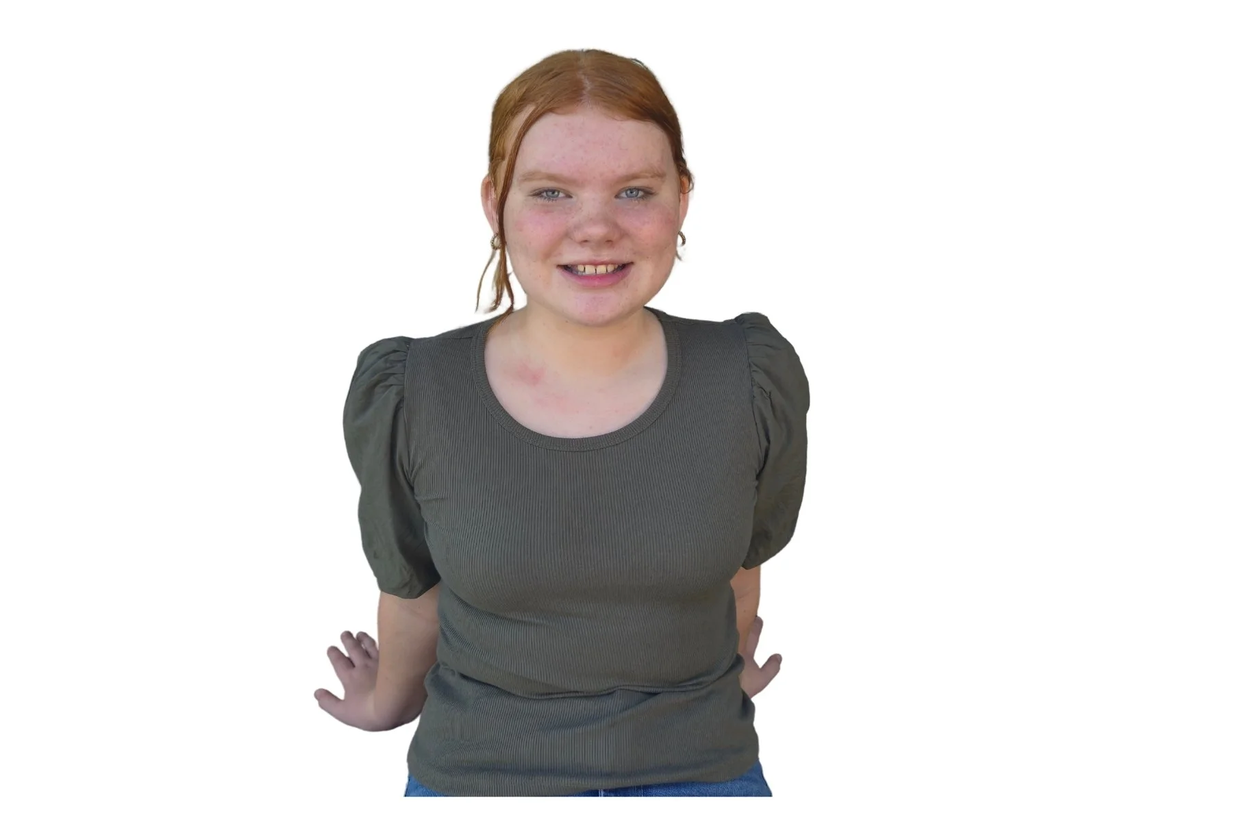 A young girl with red hair and freckles smiling, wearing a dark green top with puffed sleeves, standing with hands behind her back on a white background.