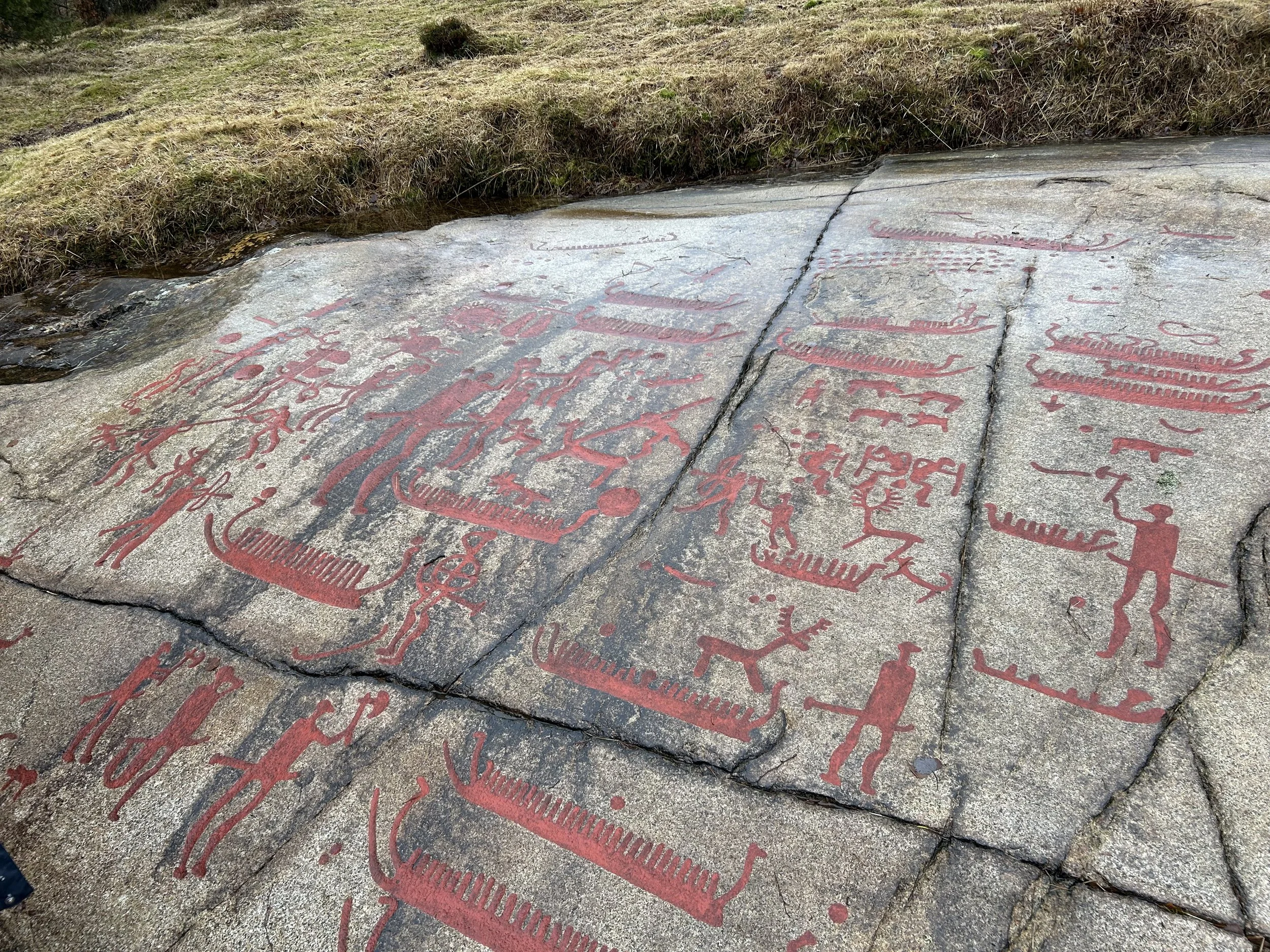 Ancient petroglyph carvings on a large rock surface, depicting figures, animals, and other symbols painted in red.