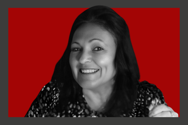 Pauline Caldaralo: Black and white photo of a smiling woman with long dark hair, wearing a patterned top, against a red background.