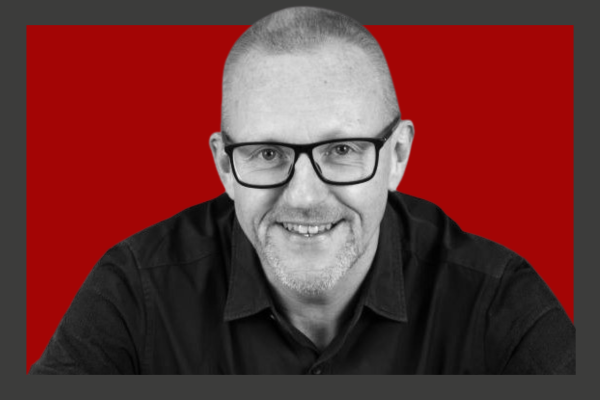 Clive Wratten: A middle-aged man with glasses, short hair, and a beard, smiling in front of a red background.