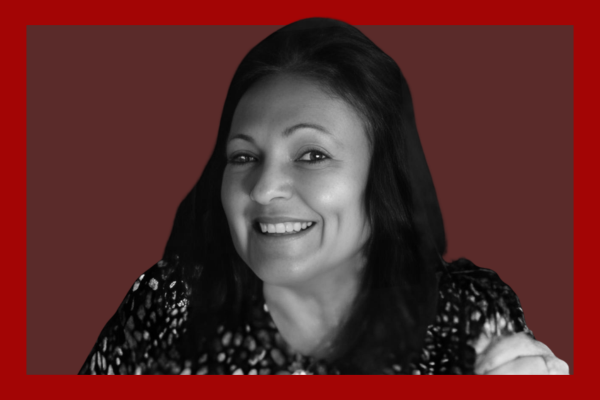Pauline Caldaralo: Black and white portrait of a smiling woman with long dark hair, wearing a patterned top, set against a dark red background.