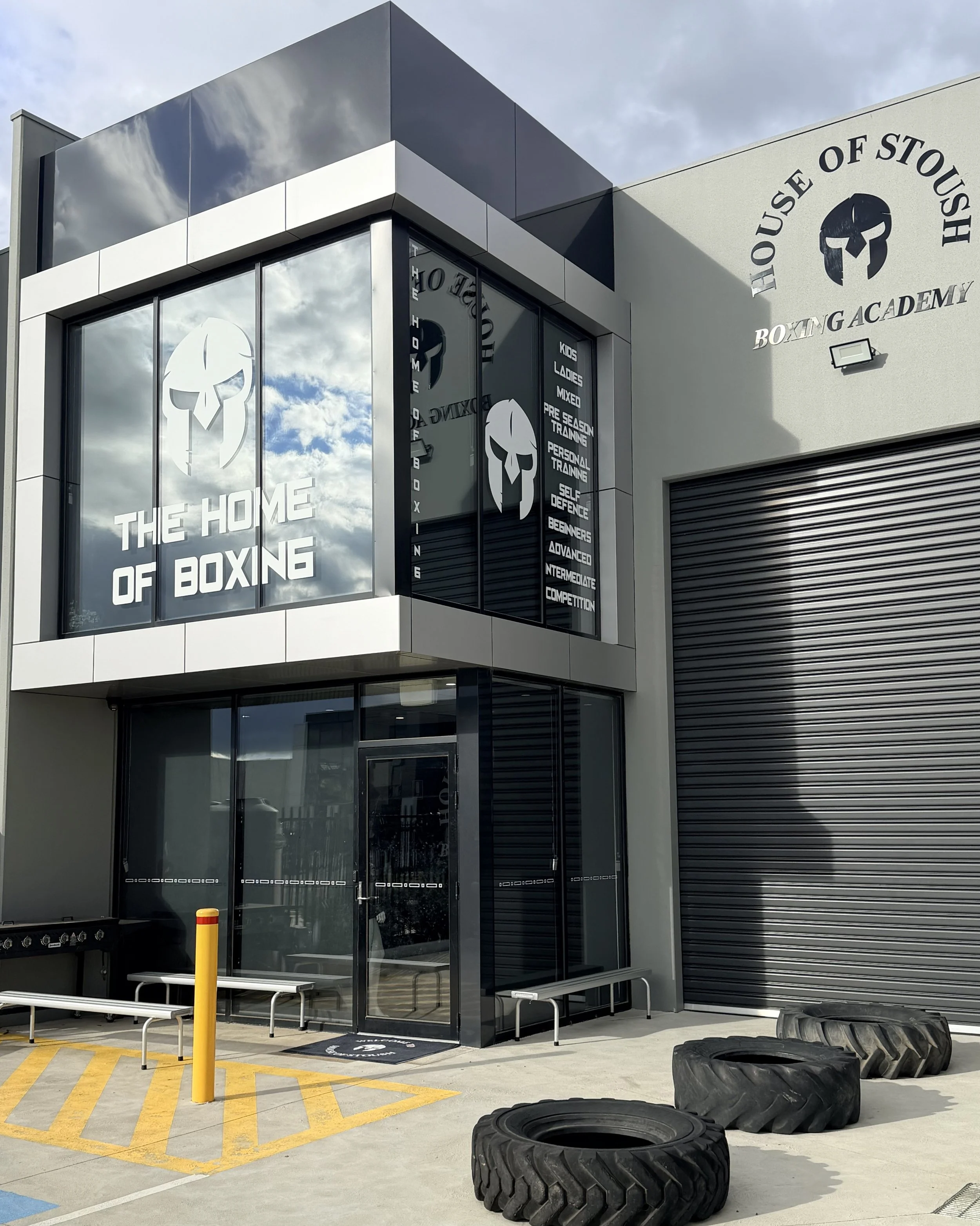 Exterior of House of Stoush "THE HOME OF BOXING" factory location. Logo of a gladiator helmet and the words "HOUSE OF STOUSH BOXING ACADEMY" on the wall. Accessible venue with disable car park, easy access and toilet facilities.