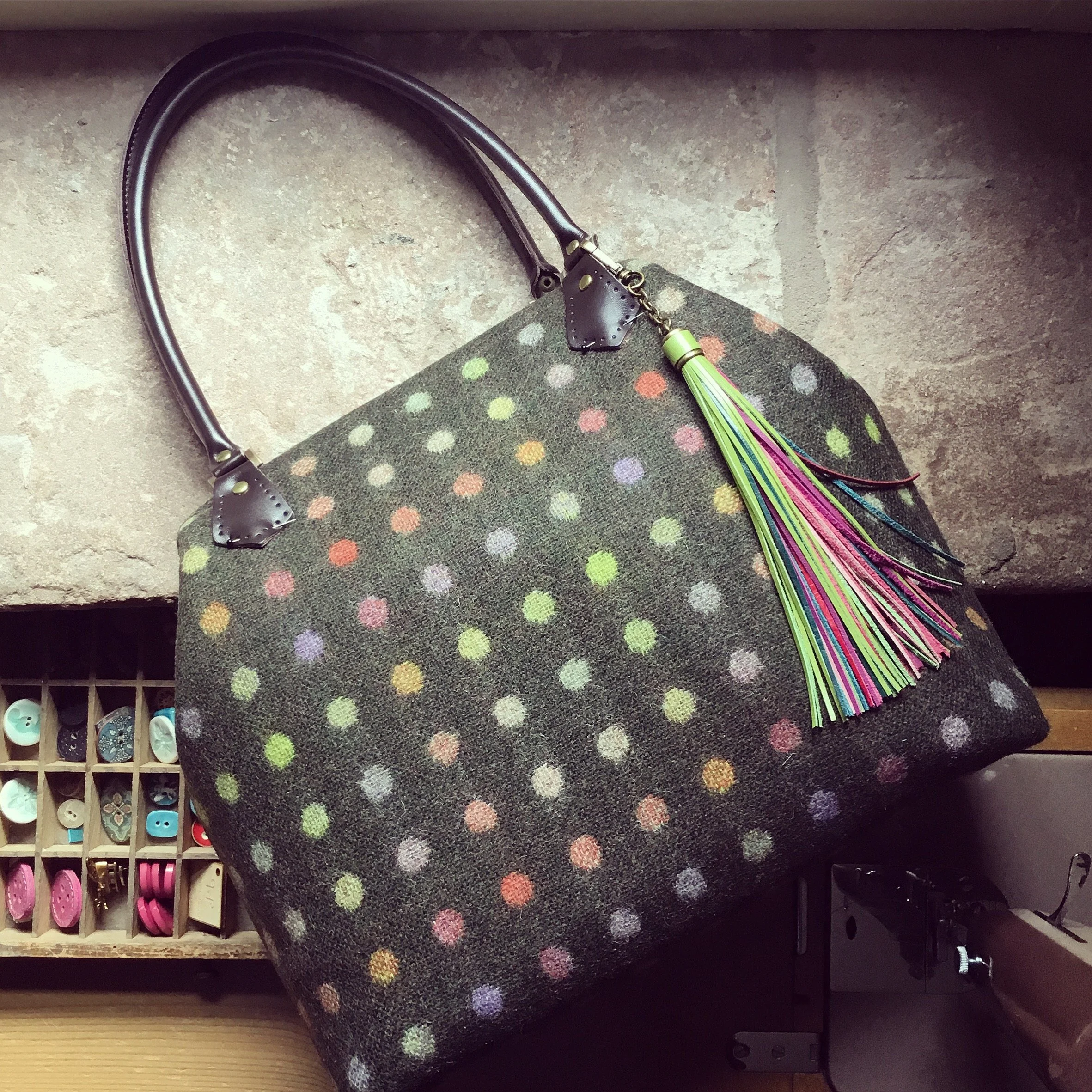 A polka dot handbag with a multicolored tassel attached, resting on a stone surface.