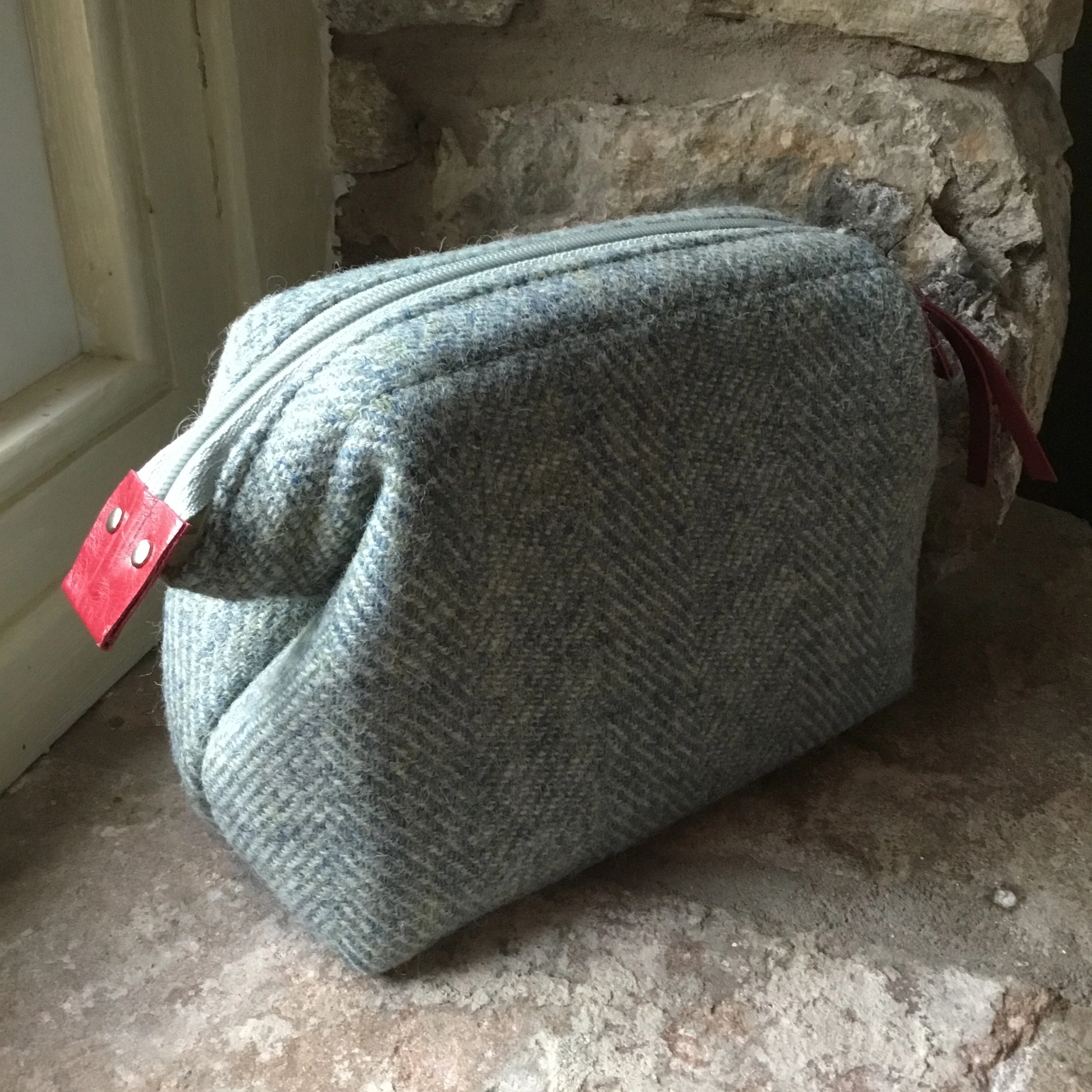 Gray tweed fabric zippered bag resting on a rustic stone and wood surface near a door.