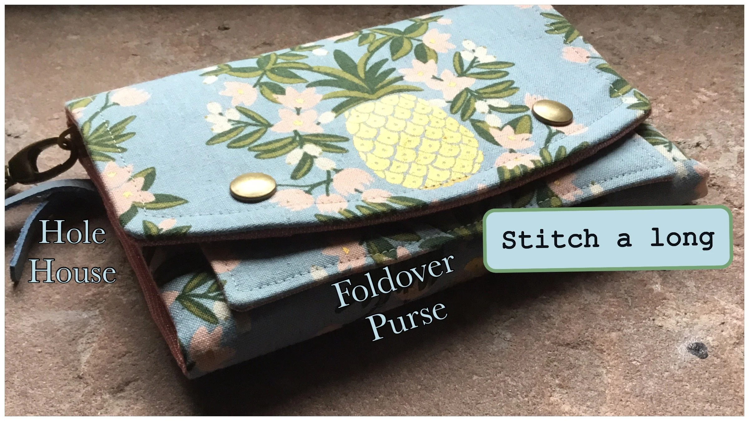 Colorful fabric purse with a pineapple and floral design, lying on a wooden surface, with labels indicating its components: Hole House, Foldover Purse, and a note to stitch it long.