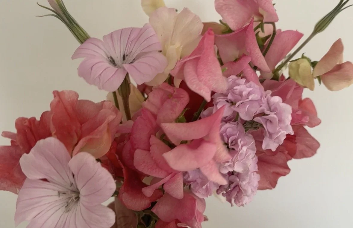 Close-up of a bouquet of pink and peach-colored flowers, including sweet peas and hydrangeas, against a neutral background.