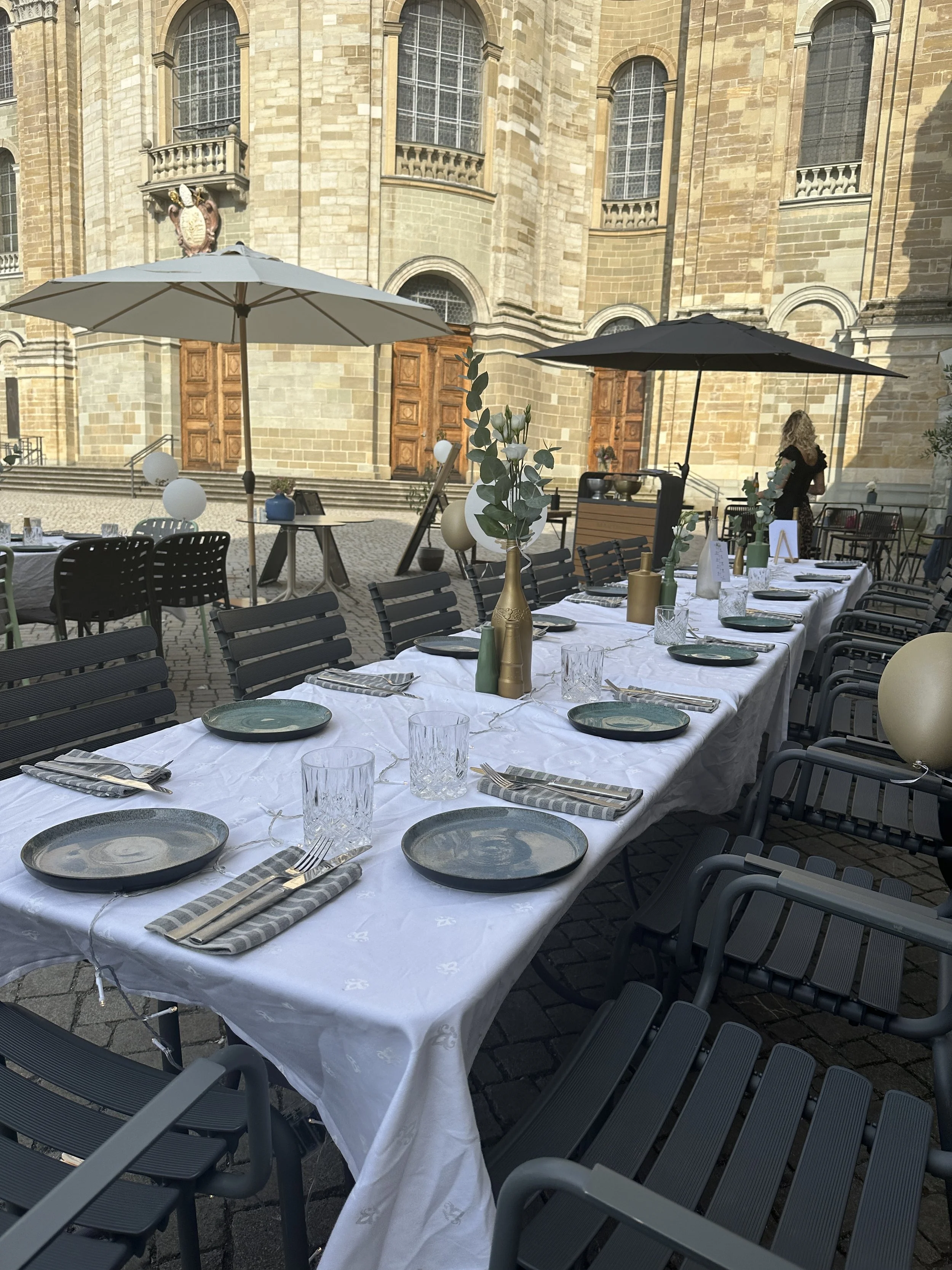 Ein festlich gedeckter Tisch im Martinus in Weingarten mit weißen Tischdecken, grün-grauen Tellern, Gläsern, Besteck und Dekorationen, vor einer historischer Kulisse.