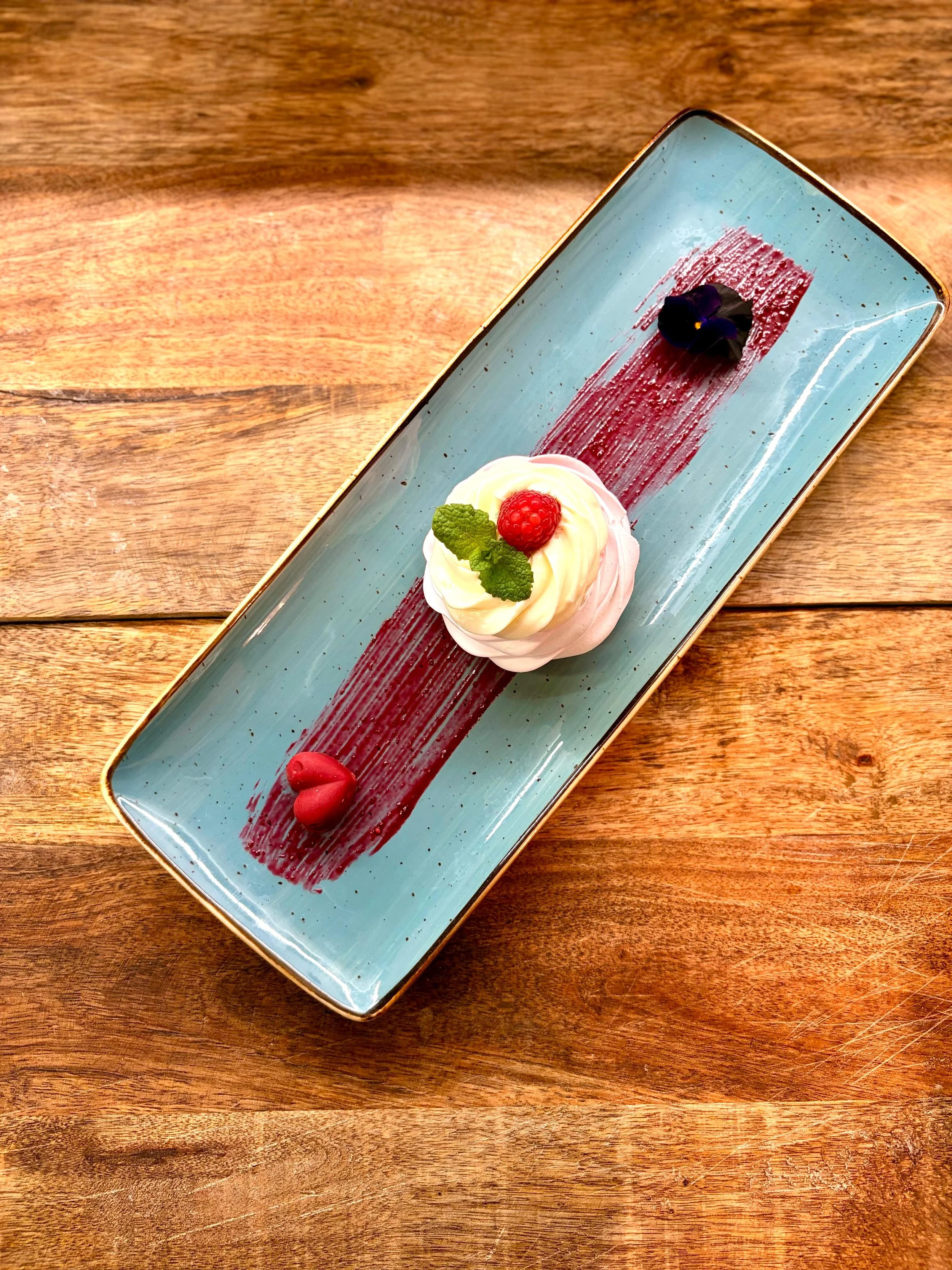 Essen im Martinus in Weingarten: Dessert mit Beeren und Minze auf einer langen, blauen Platte auf einem Holztisch.