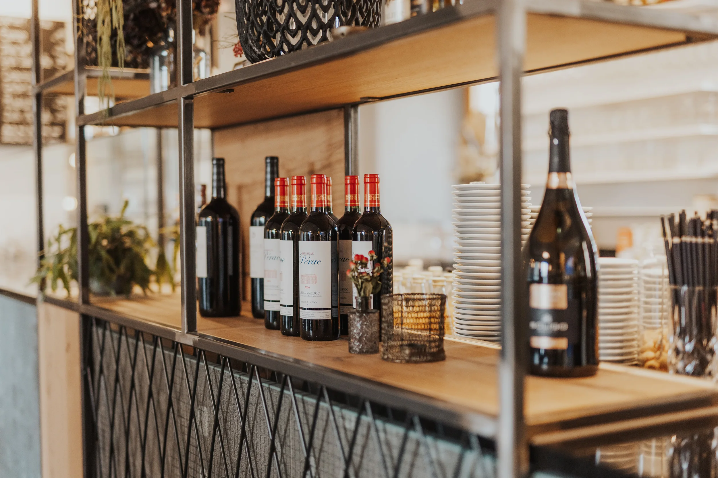 Regal mit Flaschen Rotwein, weißen Tellern und Besteck in einem Restaurant oder Café.