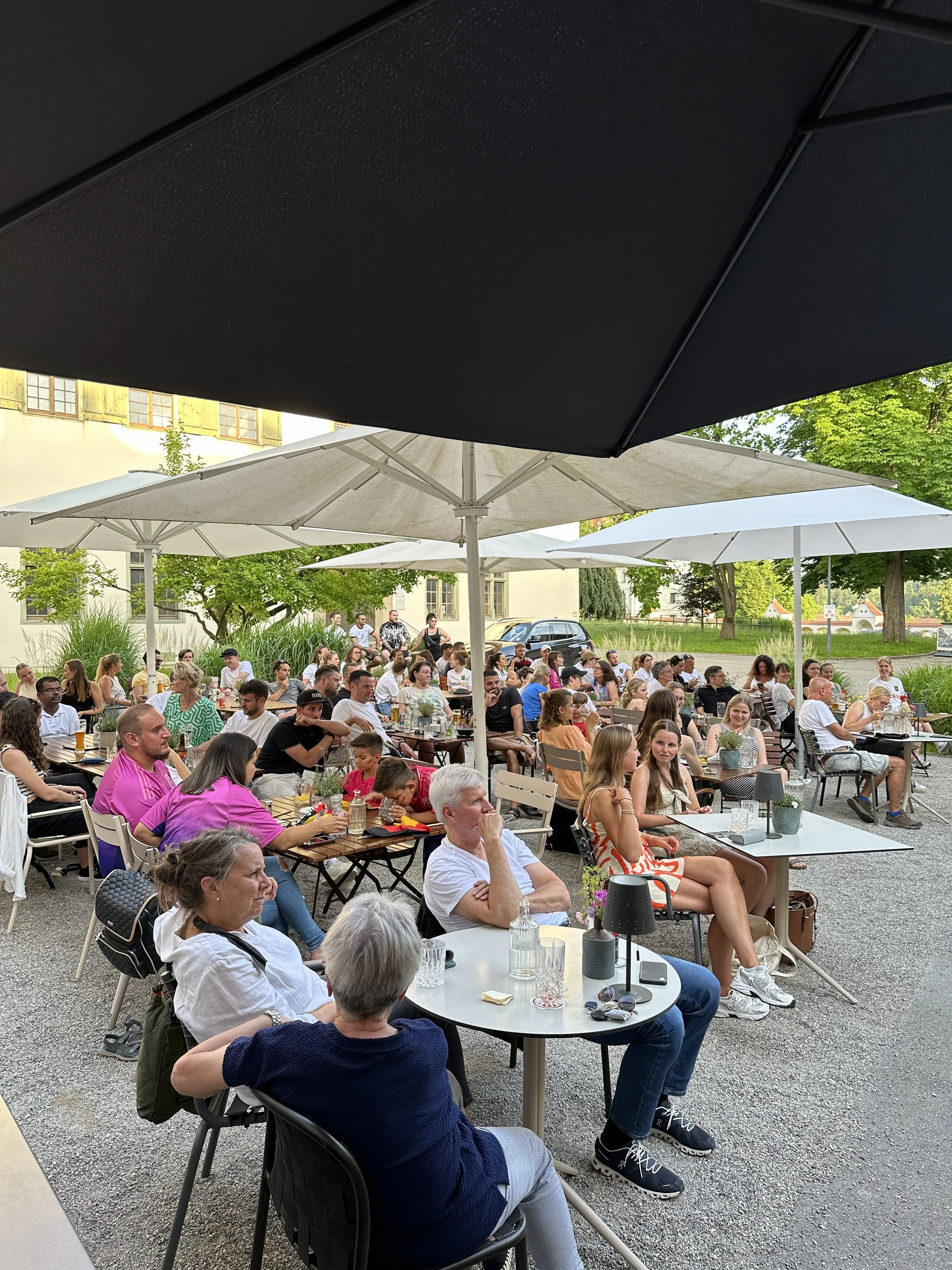 Menschen sitzen unter Sonnenschirmen im Freien im Martinus in Weingarten.