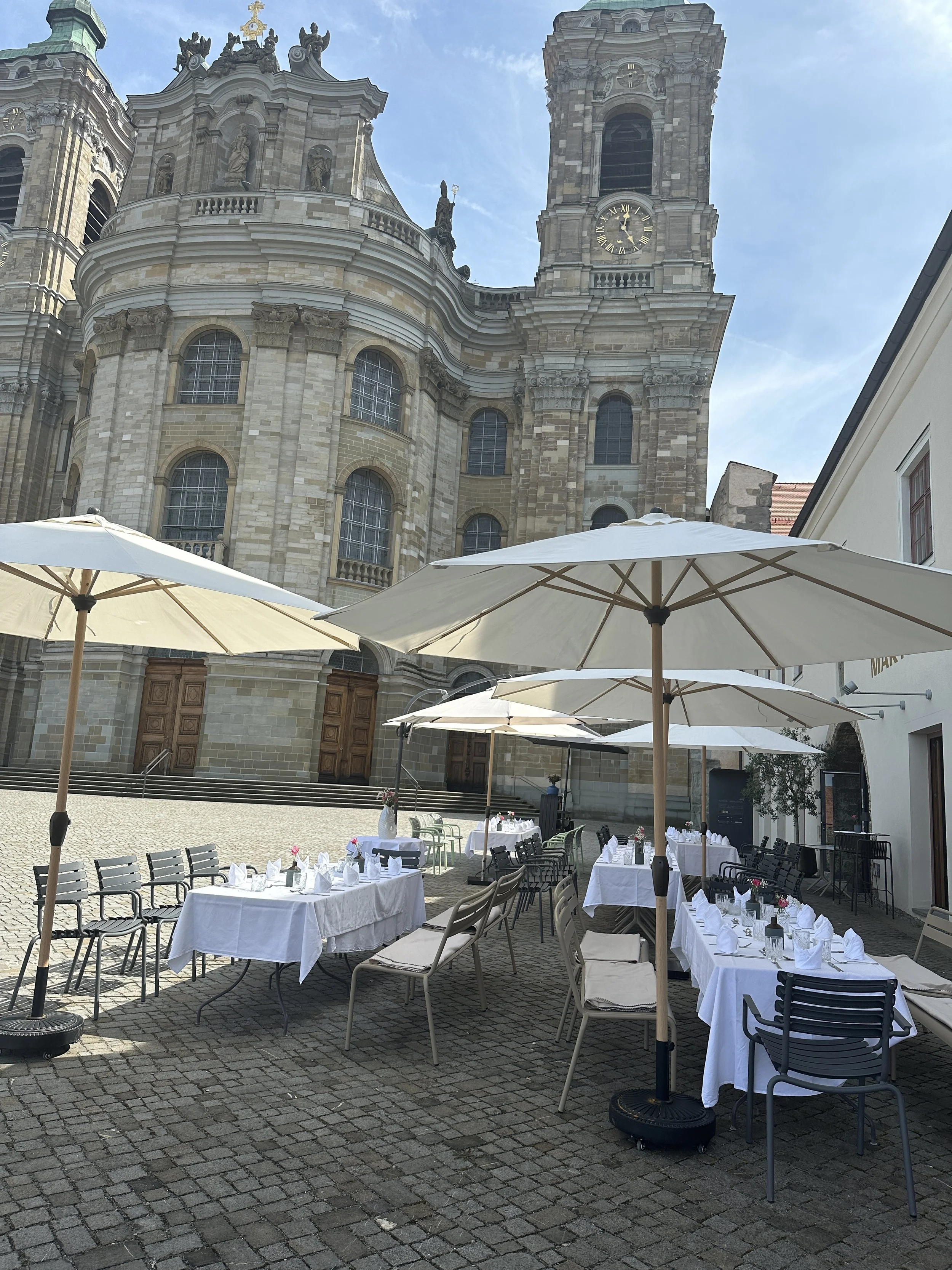 Der Außenbereich des Martinus in Weingarten mit weißen Tischen, Stühlen und Sonnenschirmen.