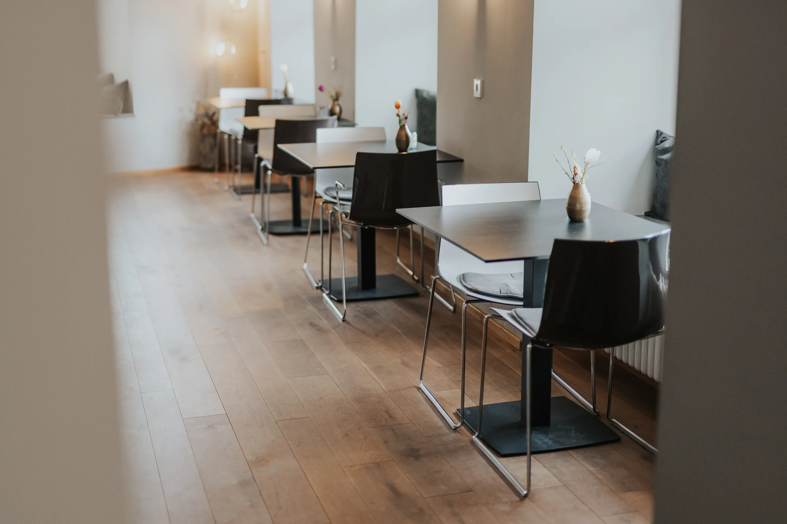 Leere Tische und Stühle im modern eingerichtetem Martinus mit Holzboden und Blumenvasen auf den Tischen.