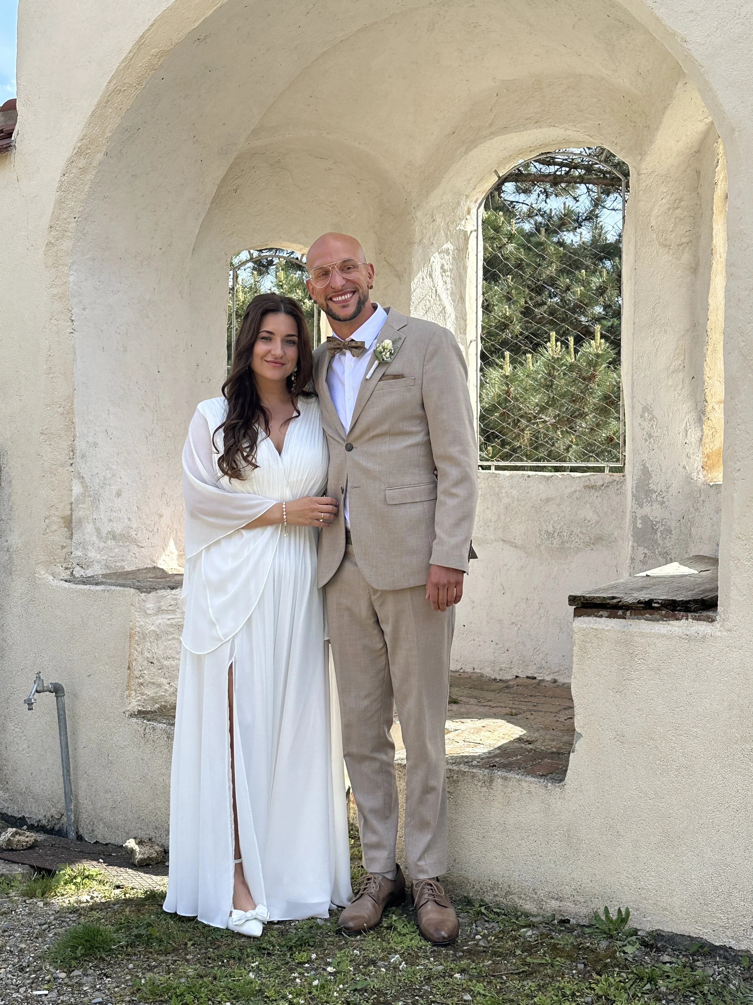 Ein junges Paar bei einer Hochzeitsfeier, stehend vor einer weißen, alten Gebäudeöffnung im Martinus in Weingarten.