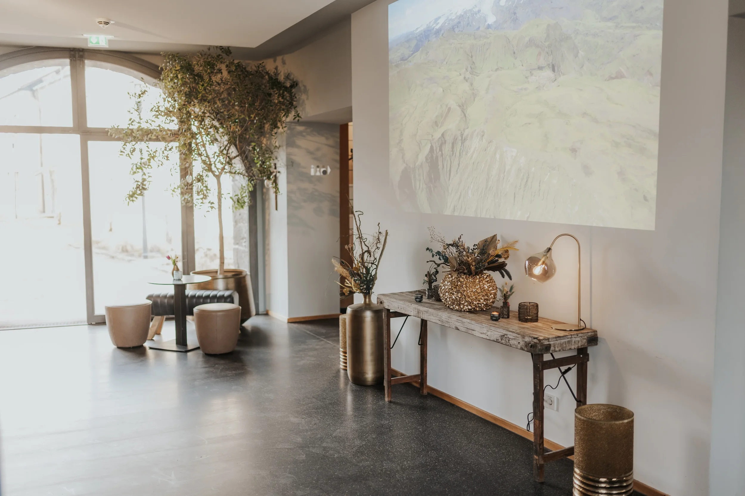 Das modernes Martinus mit großen Fenster, flauschigen Sitzpuffen und einem Holztisch. An der Wand ist ein Projektor, der eine Landschaftsbild zeigt, und stilvolle Dekorationen.