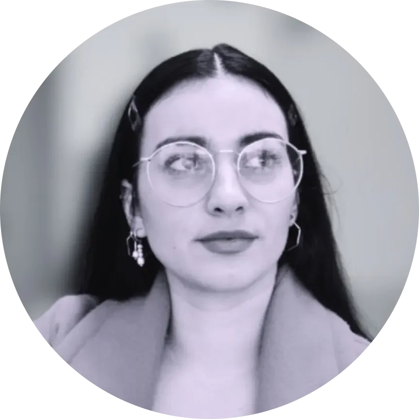 A woman with dark hair, glasses, and earrings looking to her right, wearing a blazer, in a grayscale photo.