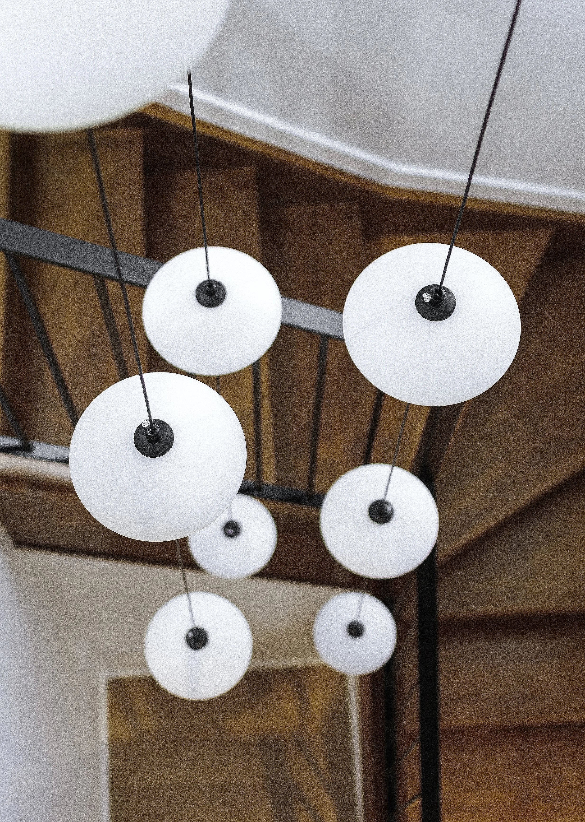 Modern ceiling light fixture with multiple white globe-shaped lights hanging from black cords over a wooden staircase.