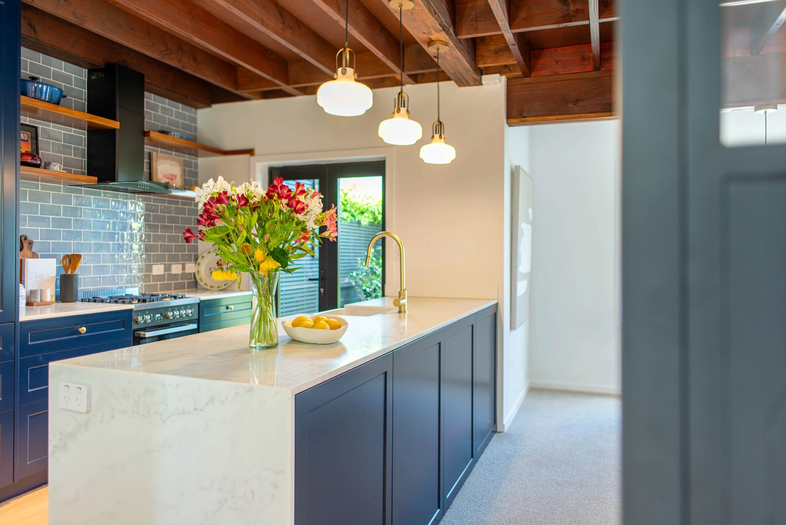 Modern kitchen with blue cabinetry, white marble island, and hanging pendant lights. Decorated with a flower vase and bowl of lemons.