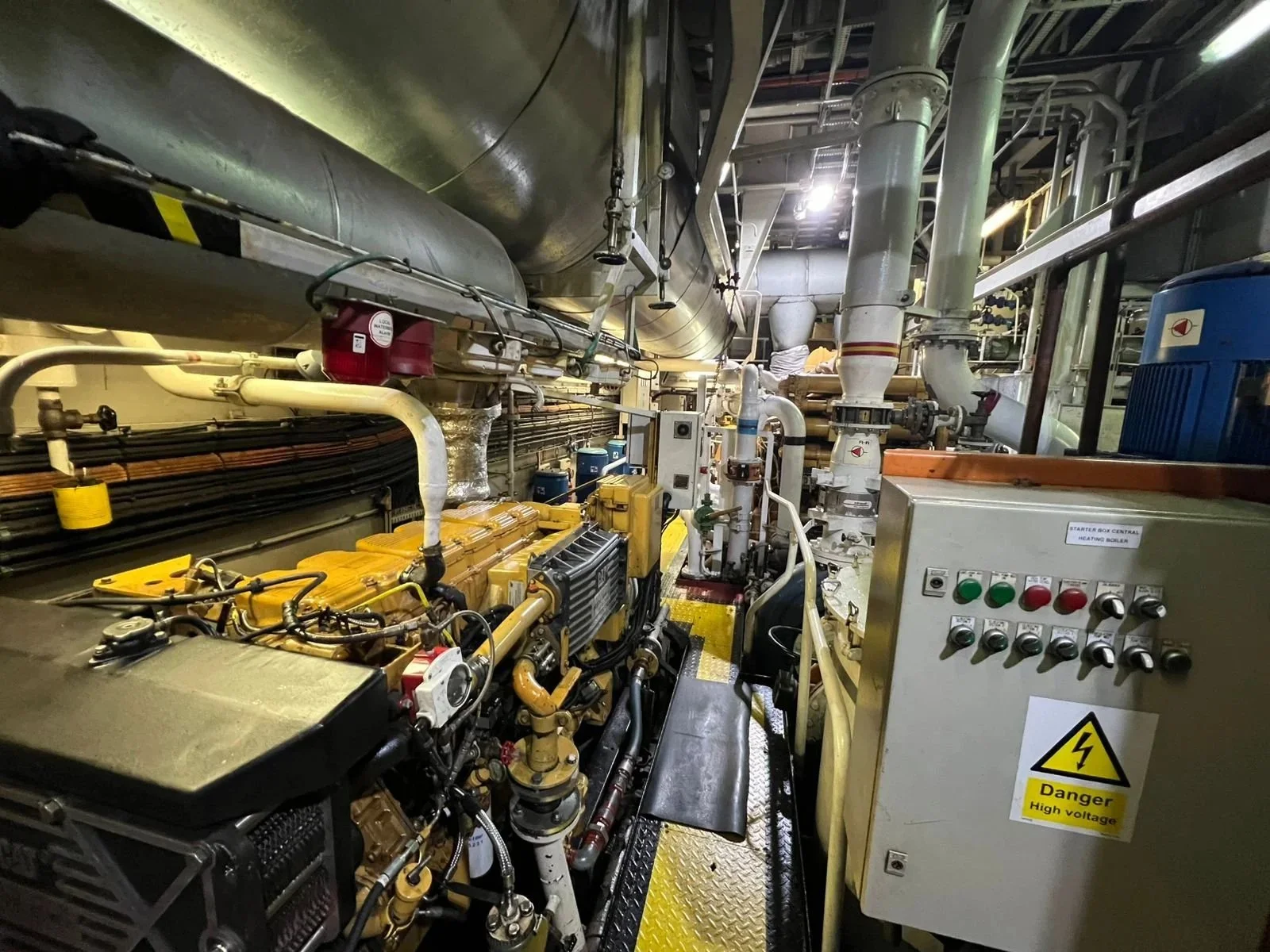 Industrial machinery with pipes, control panel, and warning sign indicating high voltage inside a facility, possibly a power plant or factory.