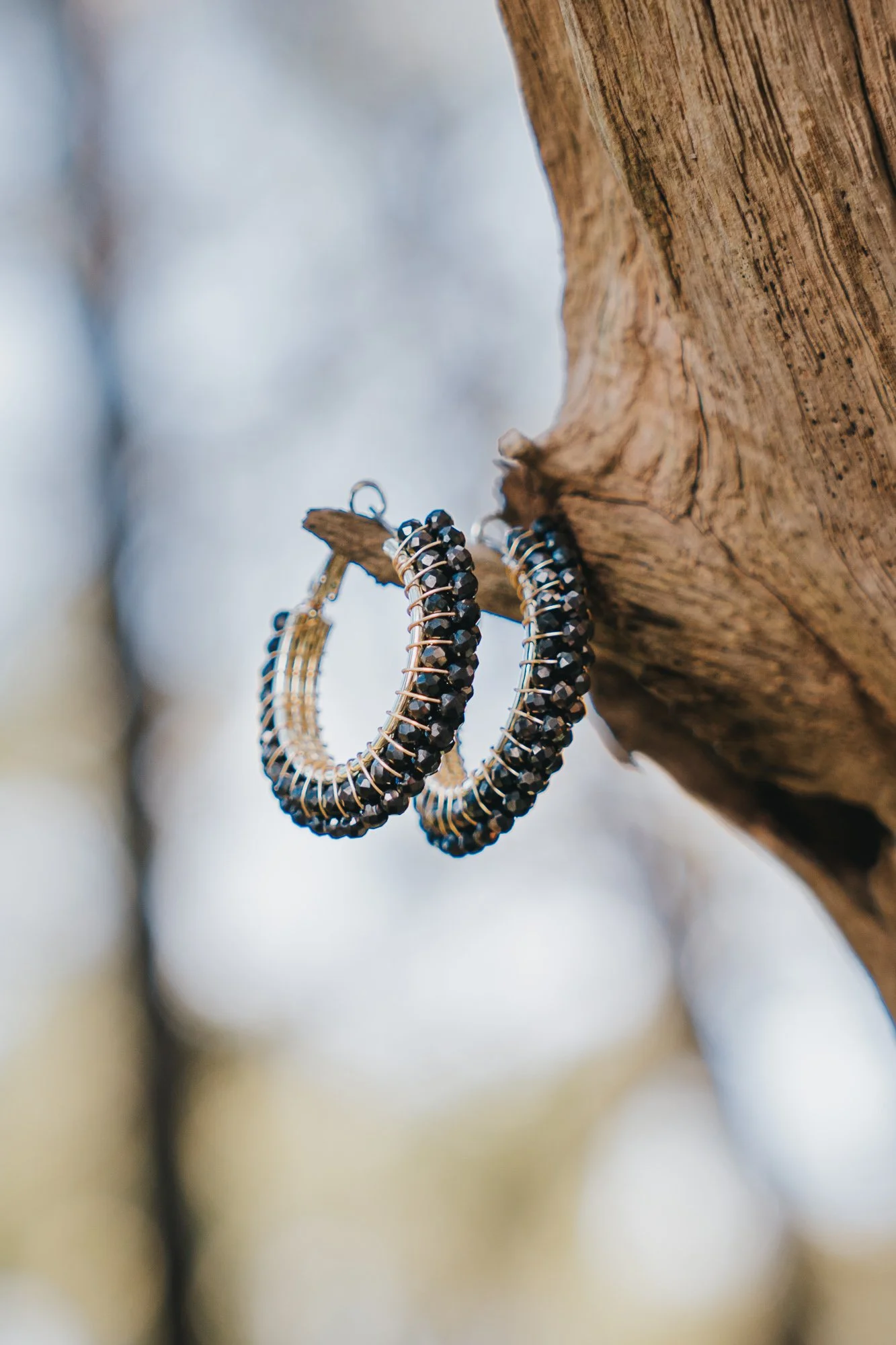 A pair of hoop earrings with black beads hanging from a tree branch.