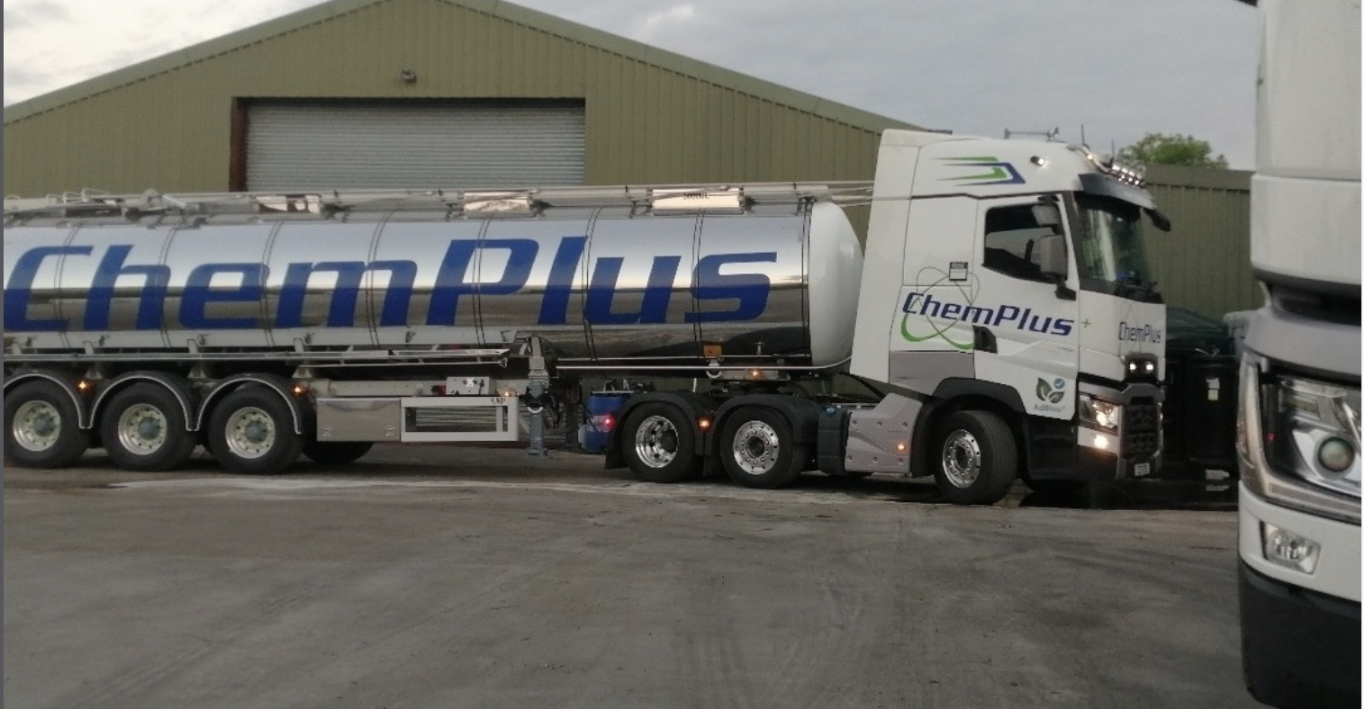 A ChemPlus tanker truck parked beside a warehouse, with a part of another truck visible on the right.