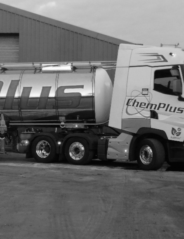 A large ChemPlus tanker truck parked on a gravel surface in front of a warehouse.