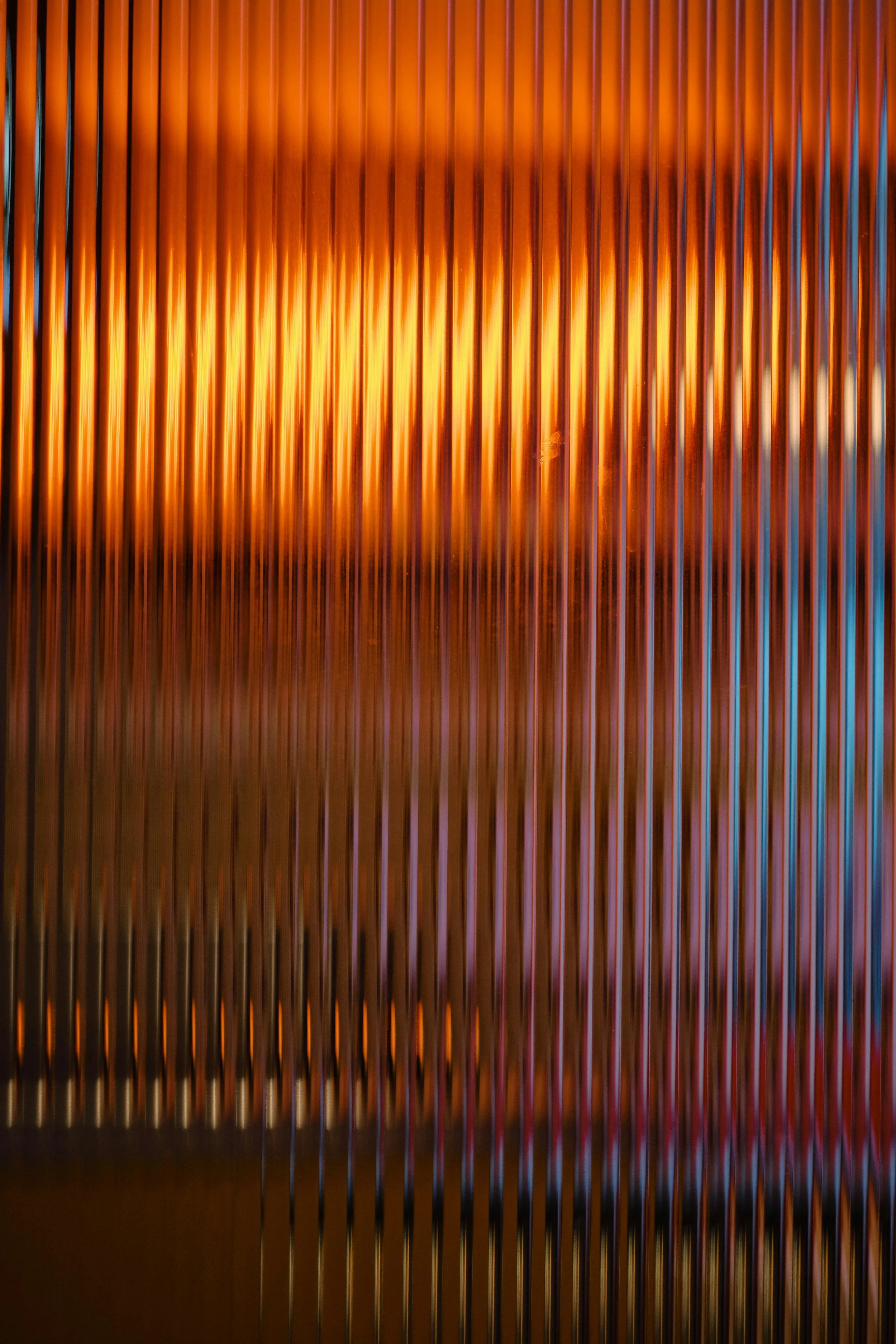 Close-up of vertical metallic bars with warm orange lighting and reflections.