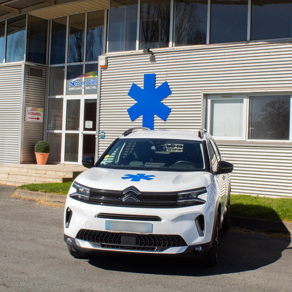 Voiture de secours stationnée devant un bâtiment médical avec un symbole d'étoile de vie bleue.