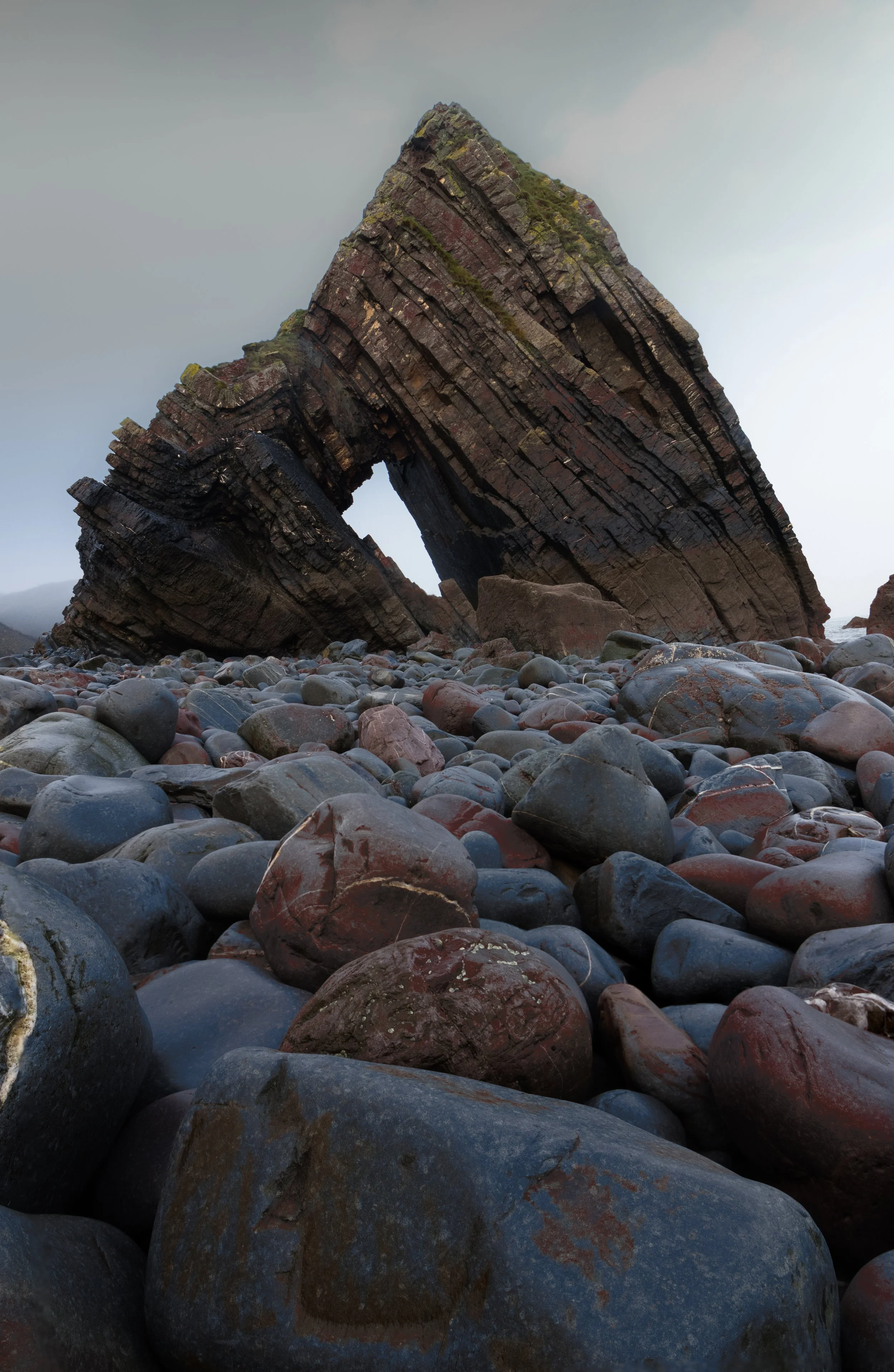 Large rock formation with a natural archway on a rocky beach.