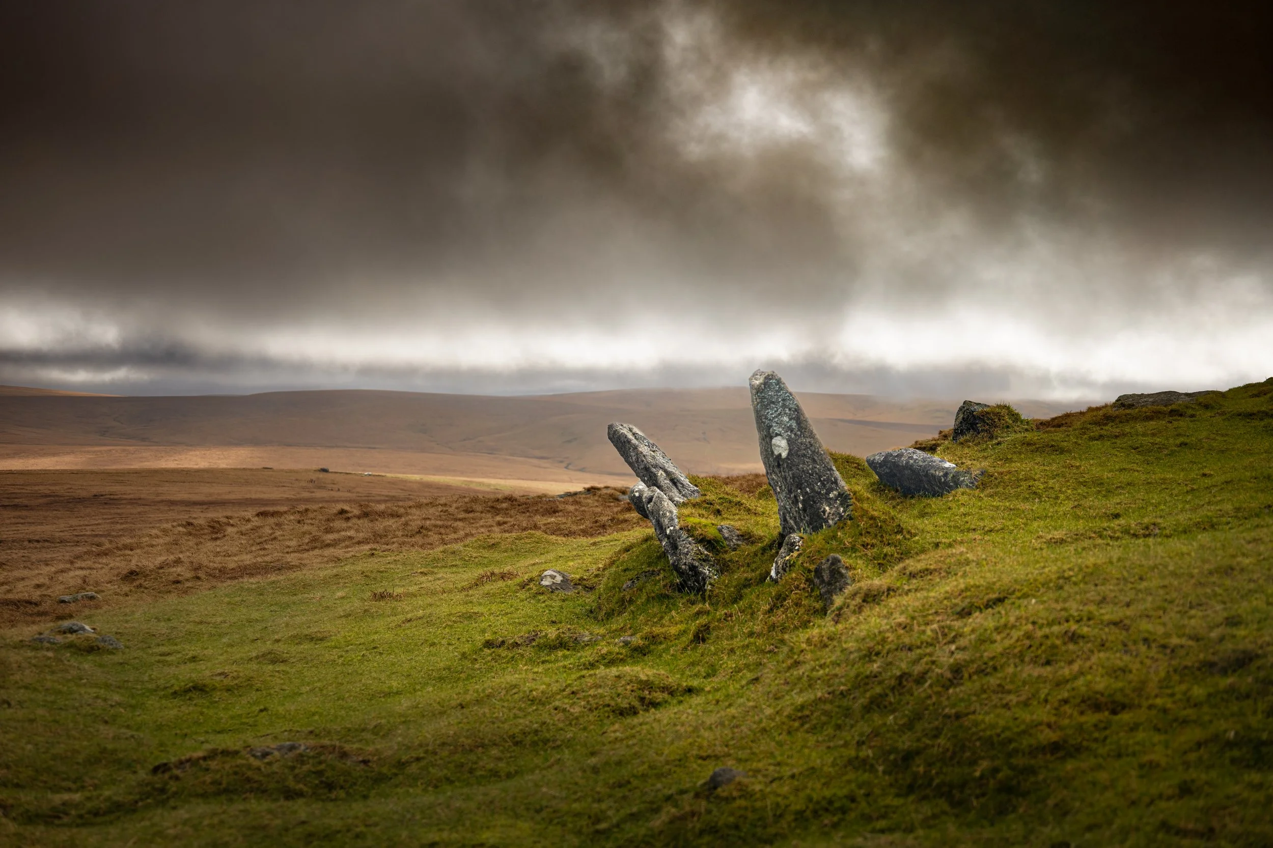 Large ancient standing stones on a grassy hillside under cloudy, overcast sky.