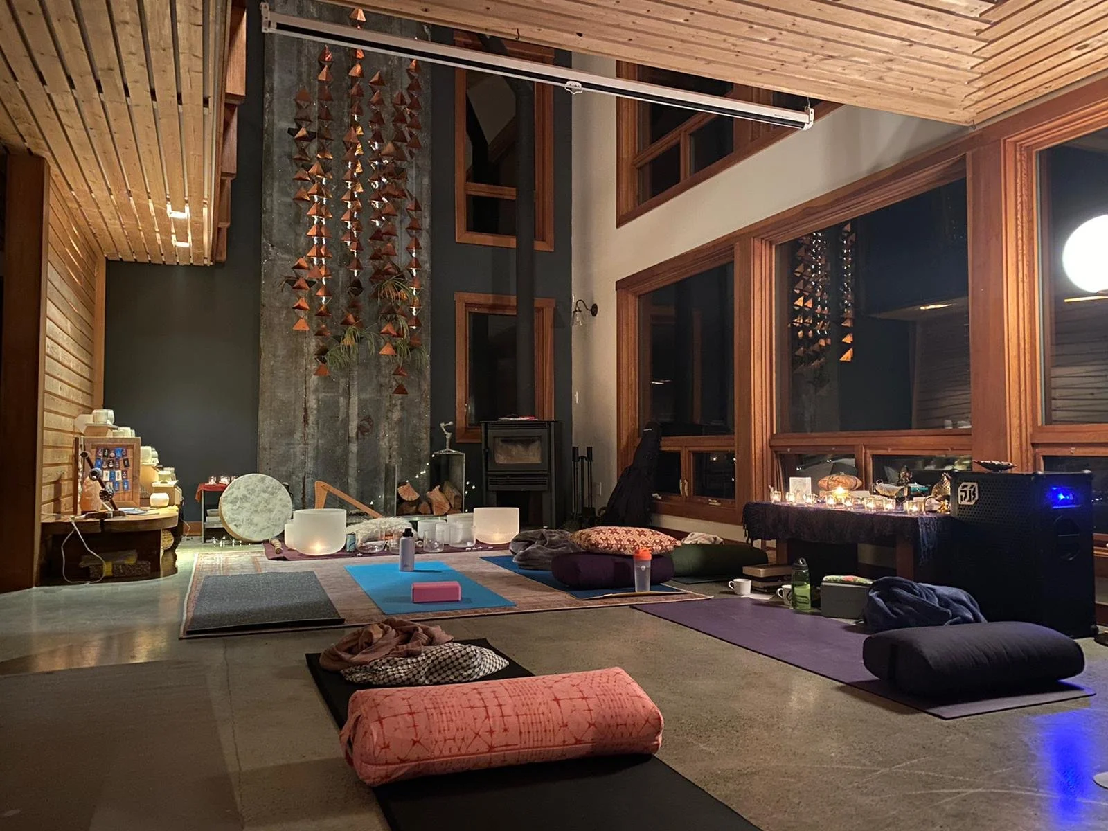 An indoor space set up for yoga or meditation with mats, cushions, and candles, featuring wooden walls and large windows.