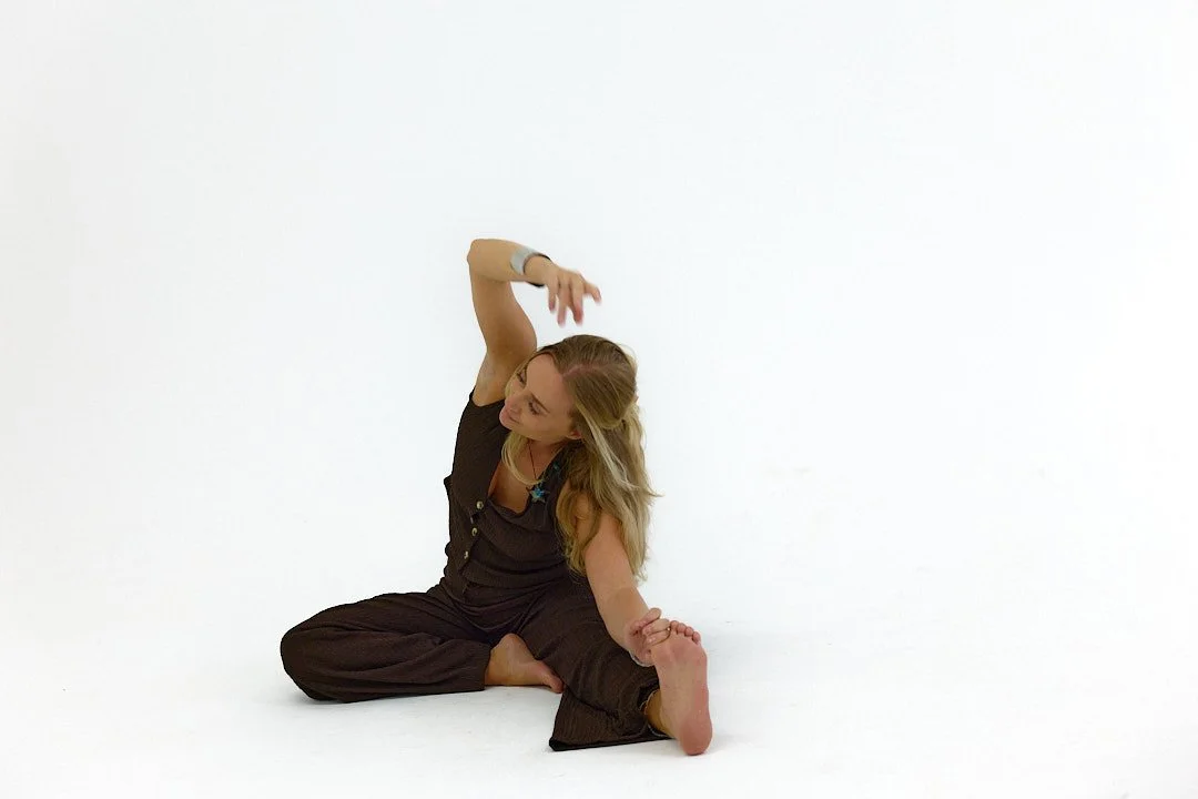 A woman with long blonde hair practicing yoga or stretching on the floor against a plain white background.