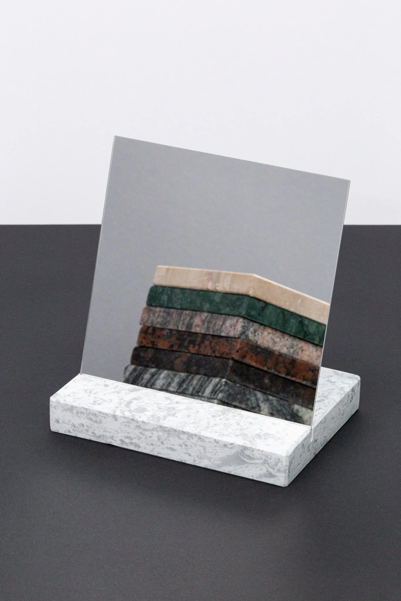 A decorative mirror with a marble base, reflecting a stack of seven different colored stones or tiles.