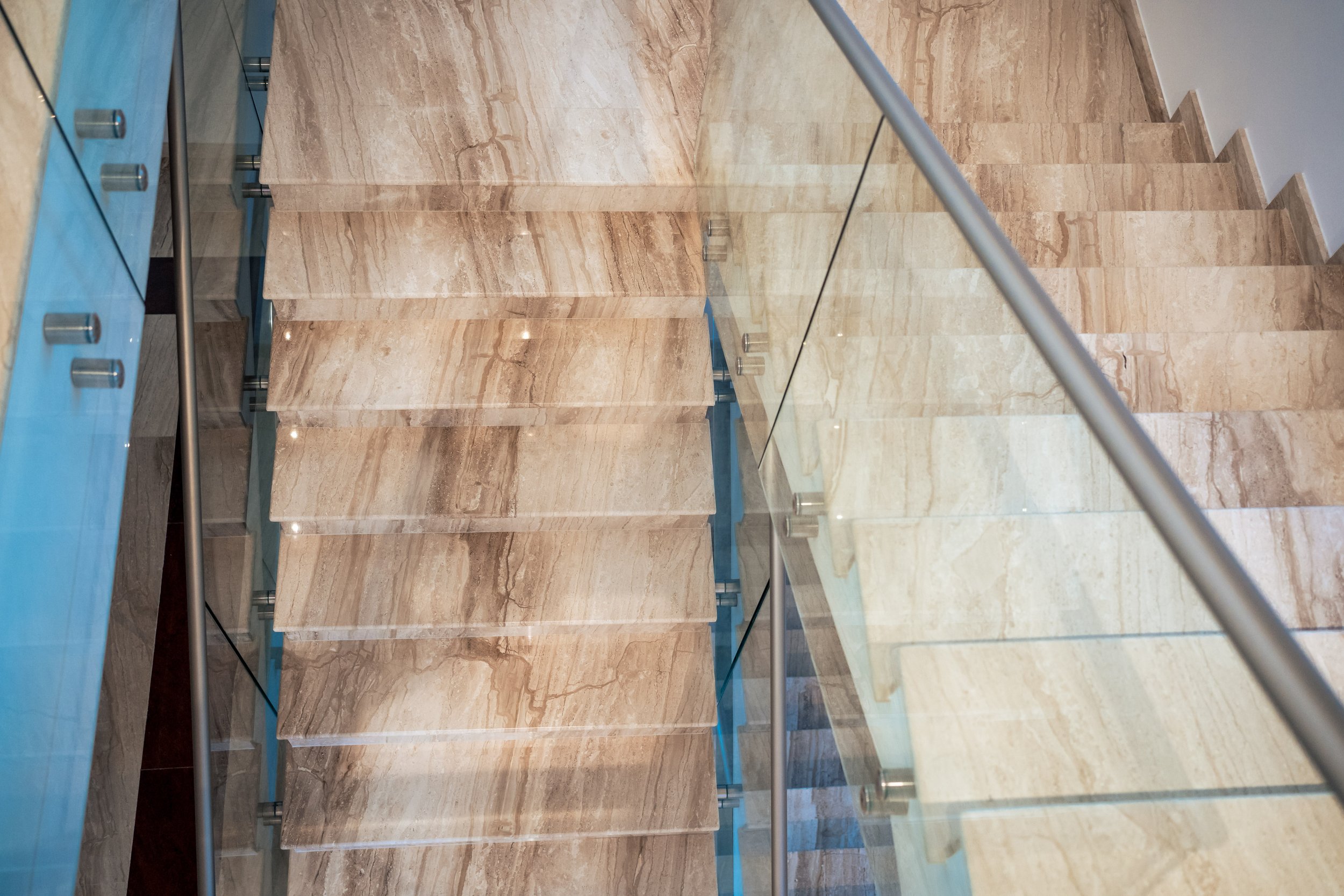 Steep marble staircase with glass and metal railing in a modern building.
