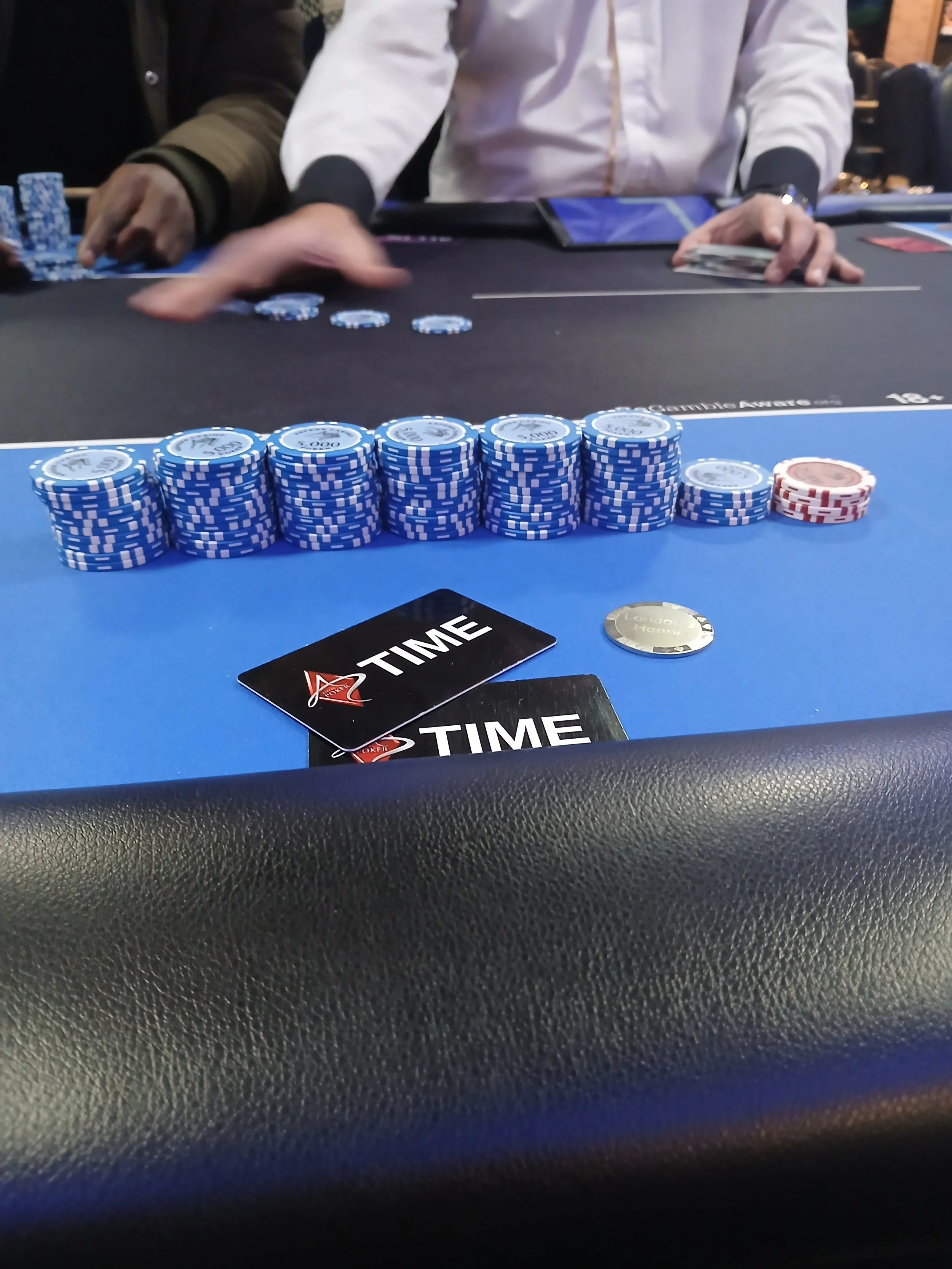 Stacks of poker chips and playing cards on a blackjack table, with players' hands visible.