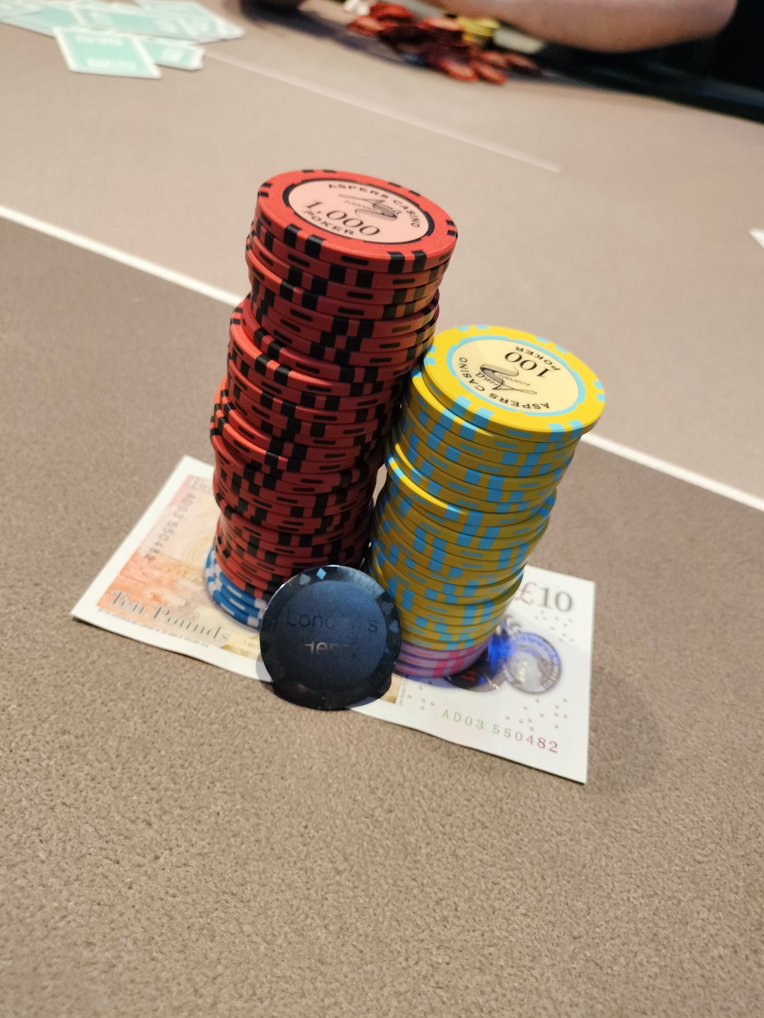 A stack of various poker chips on top of a ten pound banknote, placed on a table.