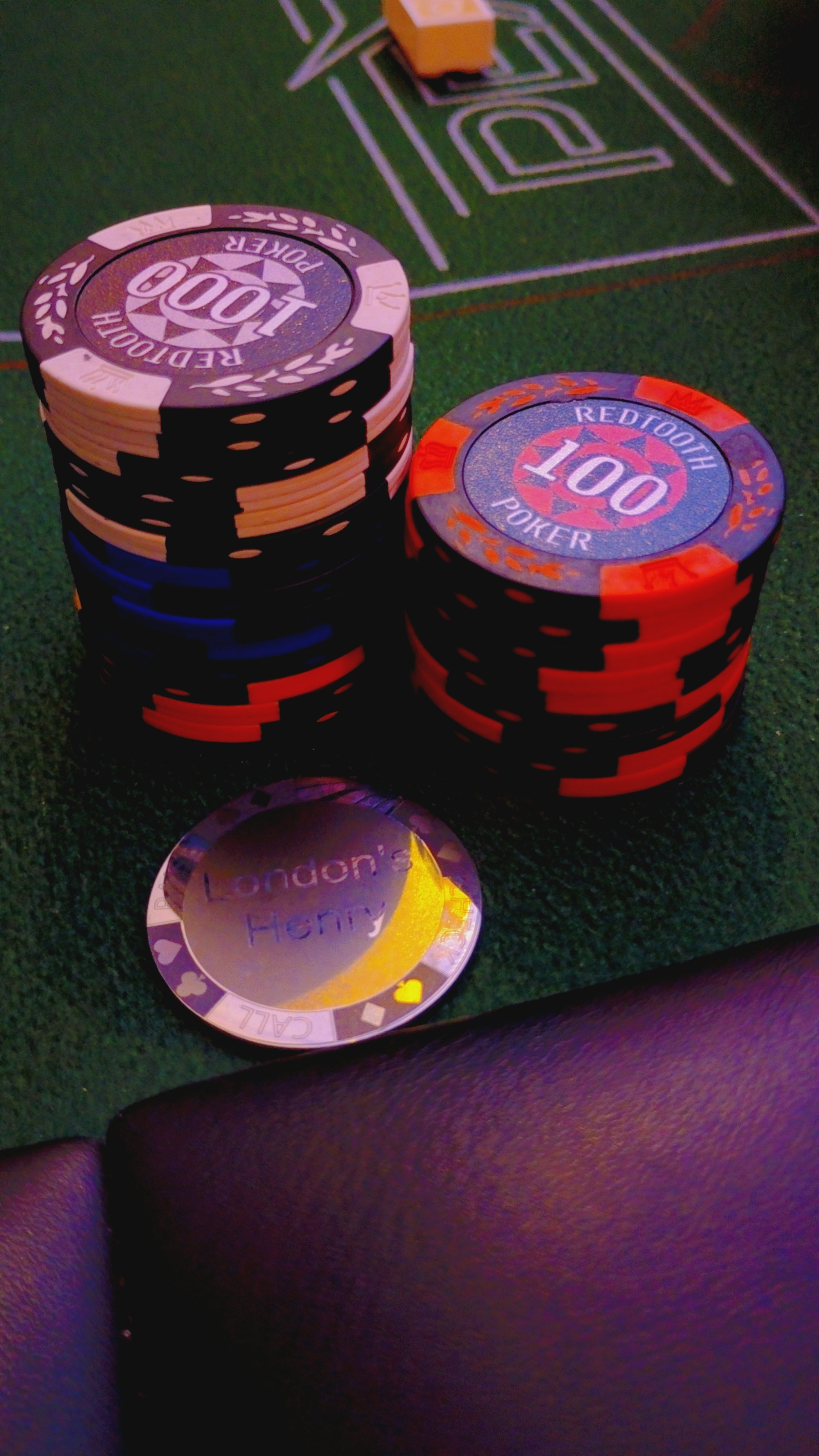 A stack of poker chips on a green poker table with a small silver coin in the foreground. The chips are purple, black, and orange, with face values of 100.