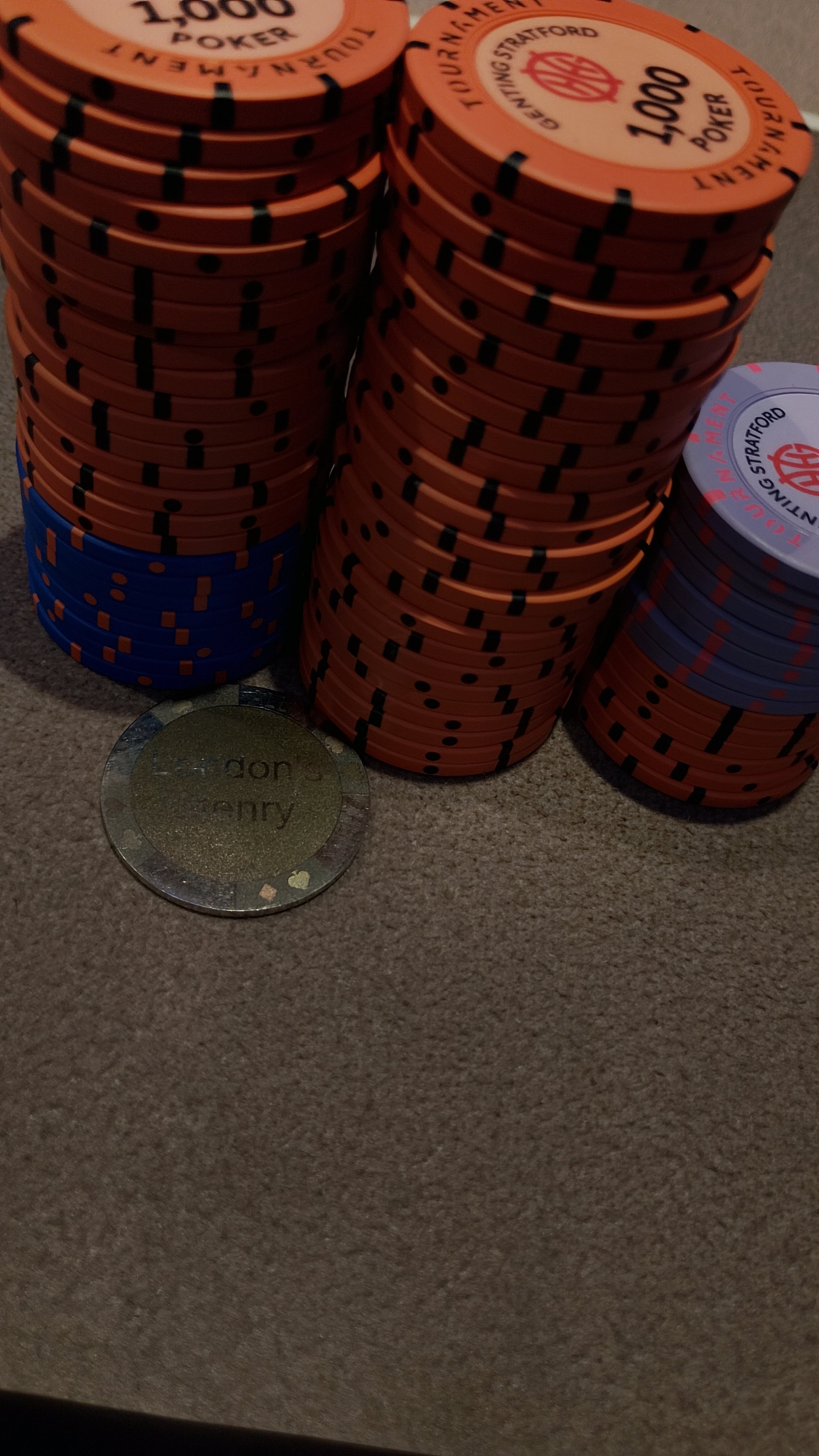 Stacks of poker chips in orange, blue, and purple colors on a table, with a small circular gold token labeled 'lizard' in front.
