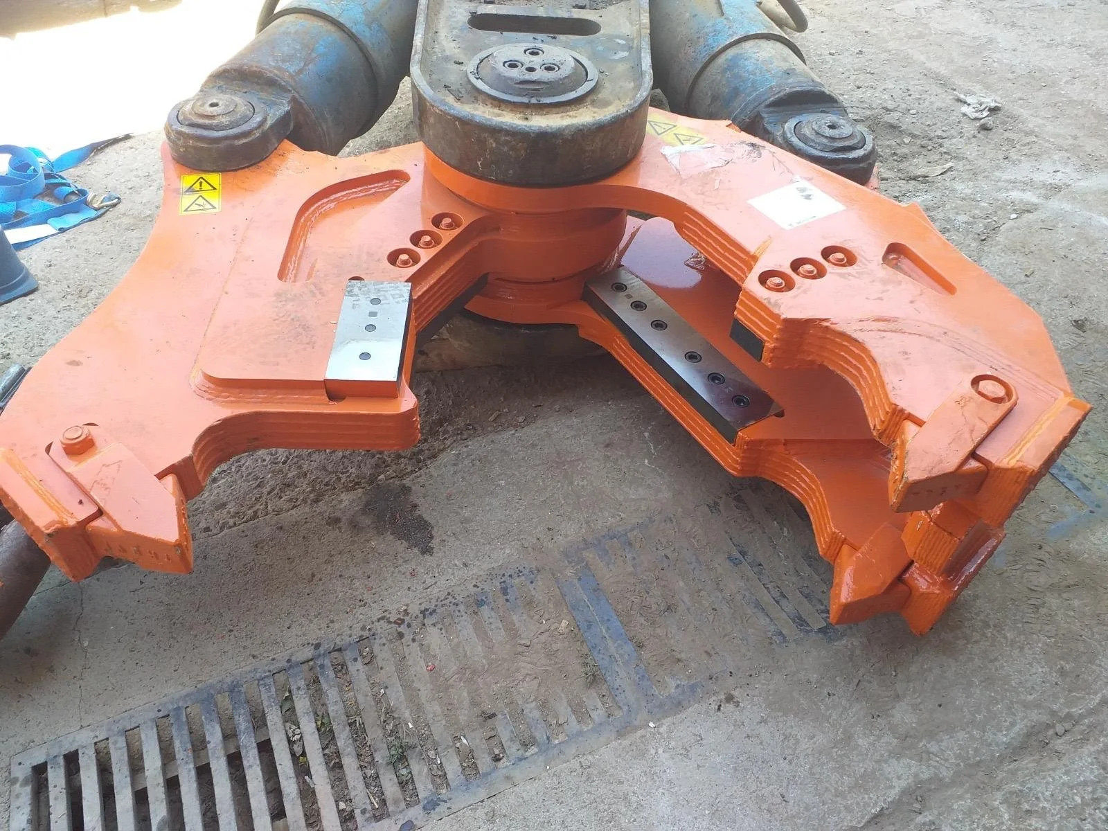 Componentes metálicos de maquinaria pesada, pintados de color naranja, en un área de construcción o taller, con herramientas y suelo de tierra.