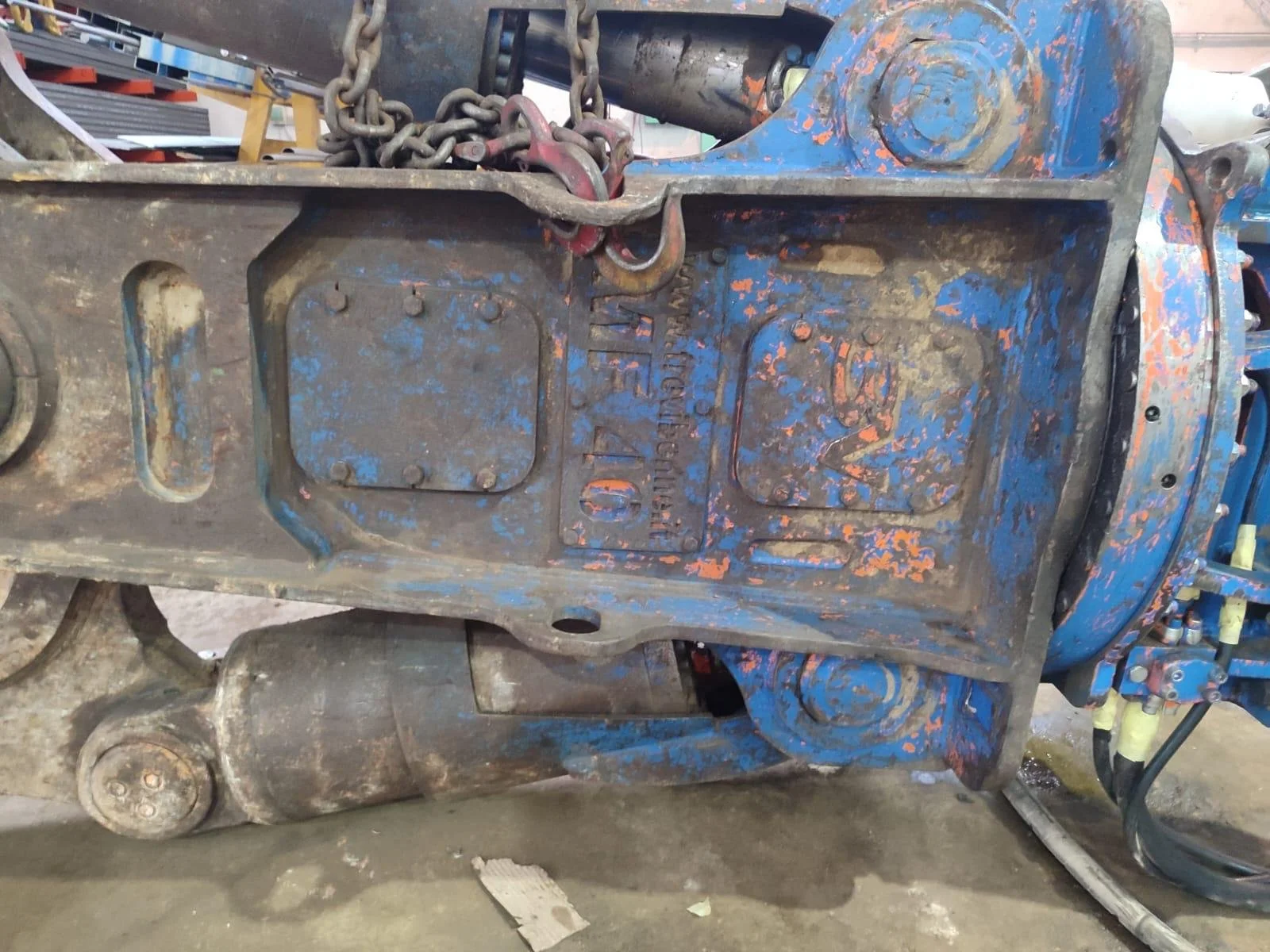 Vibrador de maquinaria industrial, azul con marcas de óxido y desgaste, con cadenas y parte del motor visible.