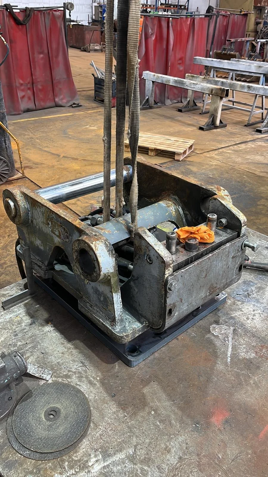 Máquina de soldar antigua y oxidada en un taller de fabricación, rodeada de herramientas y equipo de protección. 