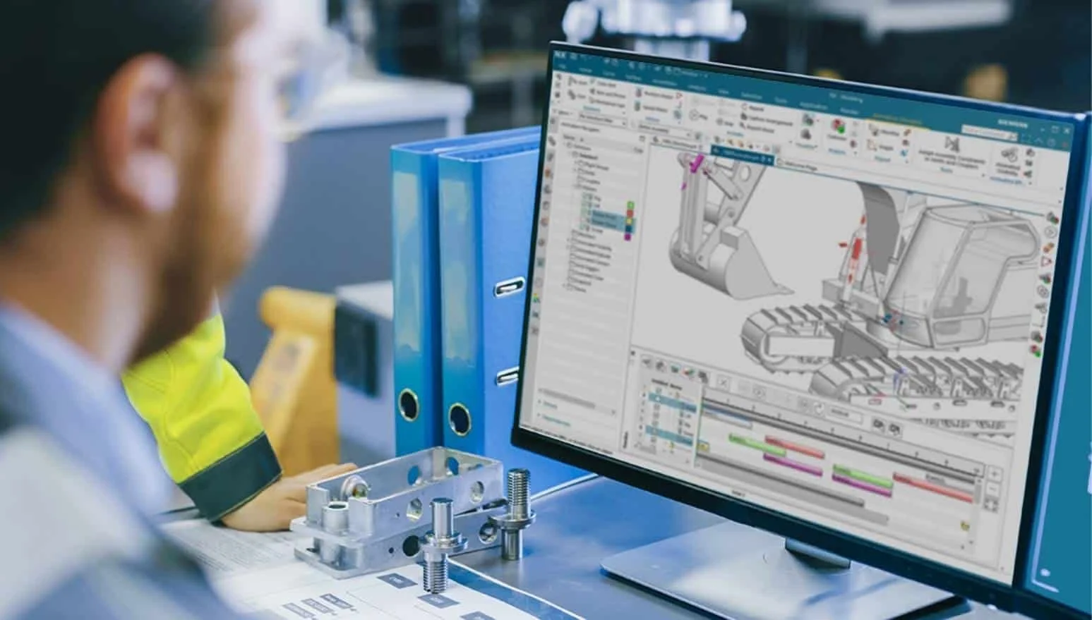 Persona trabajando en diseño de ingeniería en una computadora con software 3D, con componentes mecánicos en el escritorio.