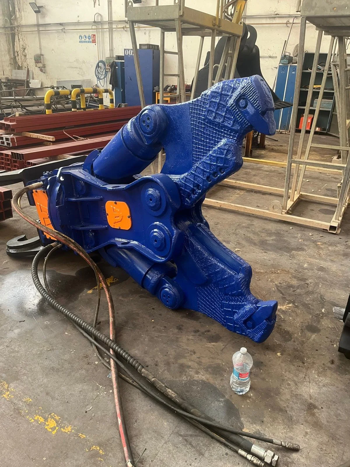 Una pieza grande de maquinaria azul en un taller de fabricación, rodeada de herramientas y otros materiales de construcción.