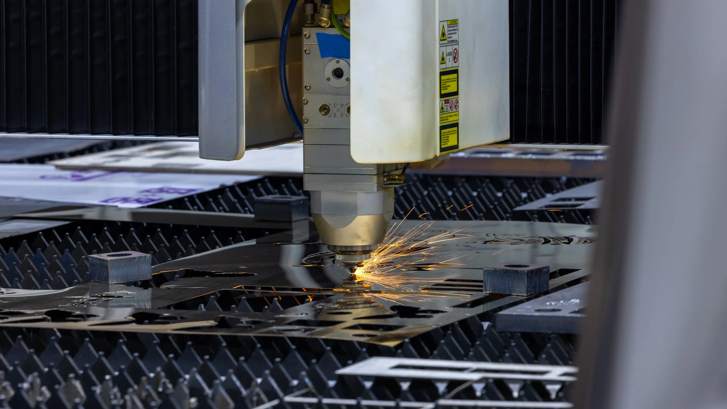 Maquina de corte láser en acción cortando metal, con chispas volando.