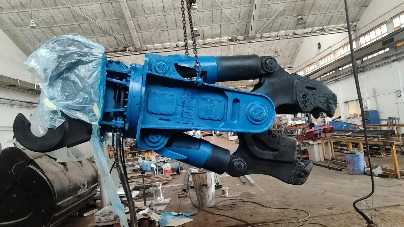 Gran brazo robótico en un taller de fabricación, con partes en azul y negro, rodeado de herramientas y maquinaria.