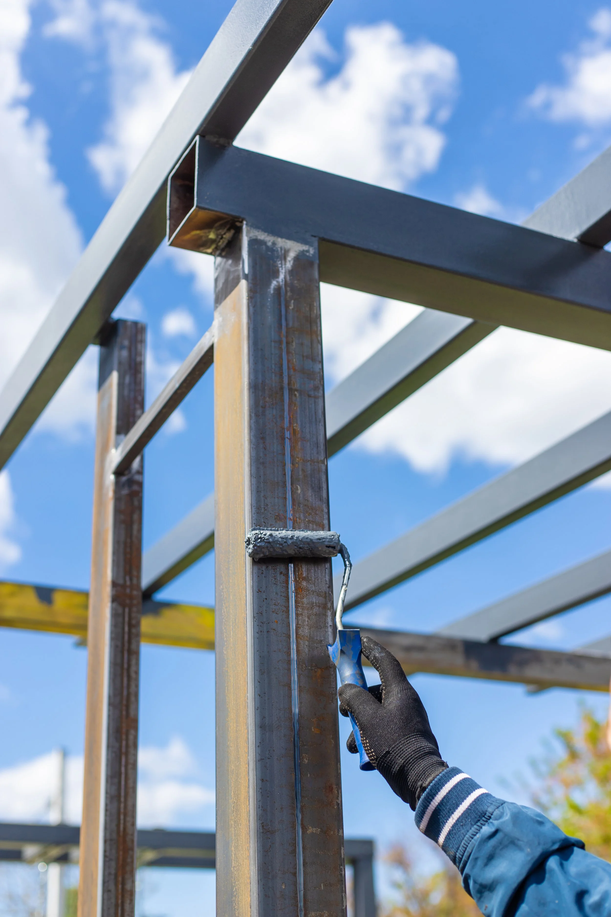 Persona pintando una estructura de metal con un rodillo en un día soleado.