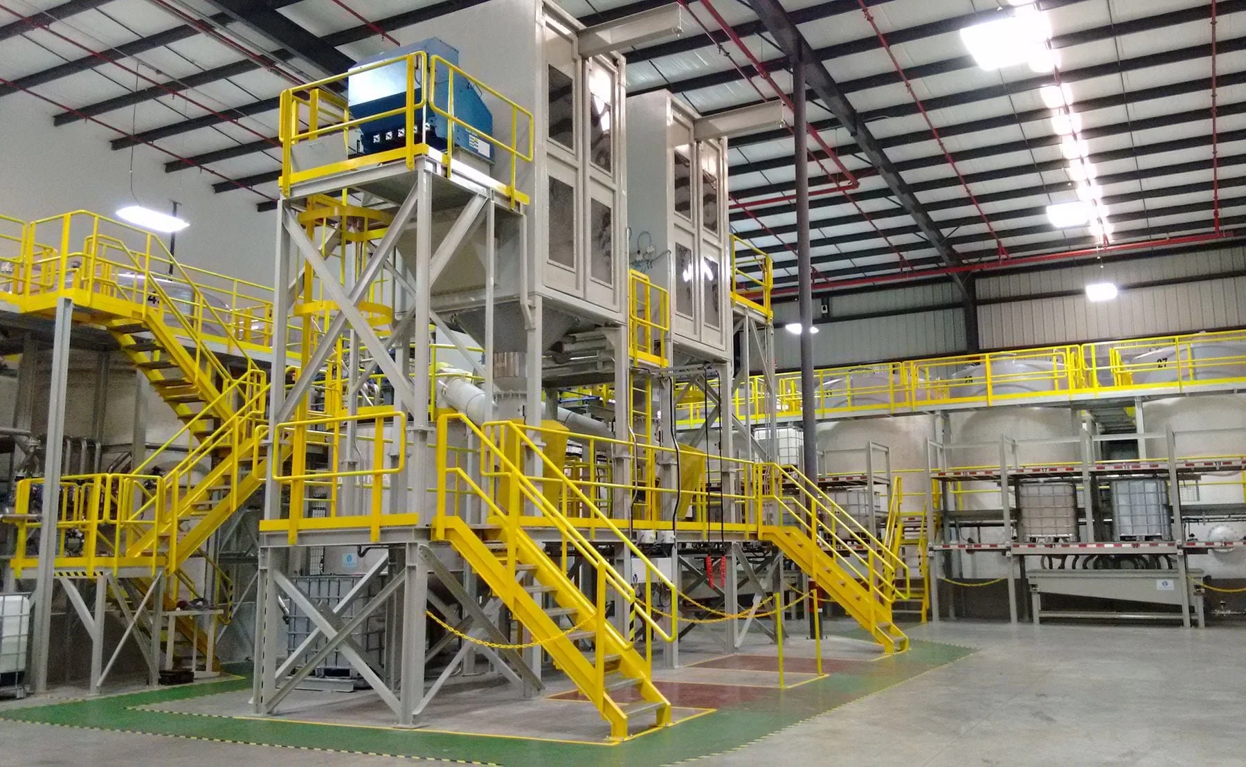 Esquema industrial con estructuras de acero, escaleras y plataformas pintadas de amarillo, dentro de una fábrica