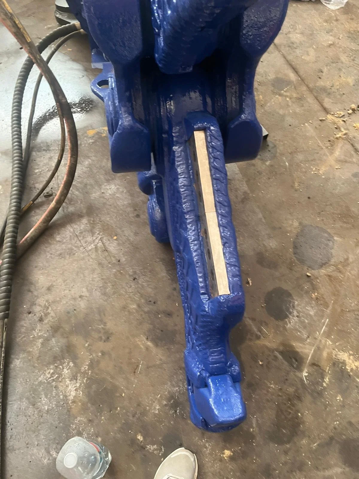 Imagen de una pieza de maquinaria azul en un taller, con una estructura metálica pintada de azul y algunos cables y una botella de agua en el suelo.