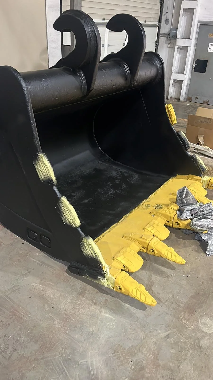 Cucharón excavadora nuevo, pintado de negro y amarillo, en un taller de construcción.
