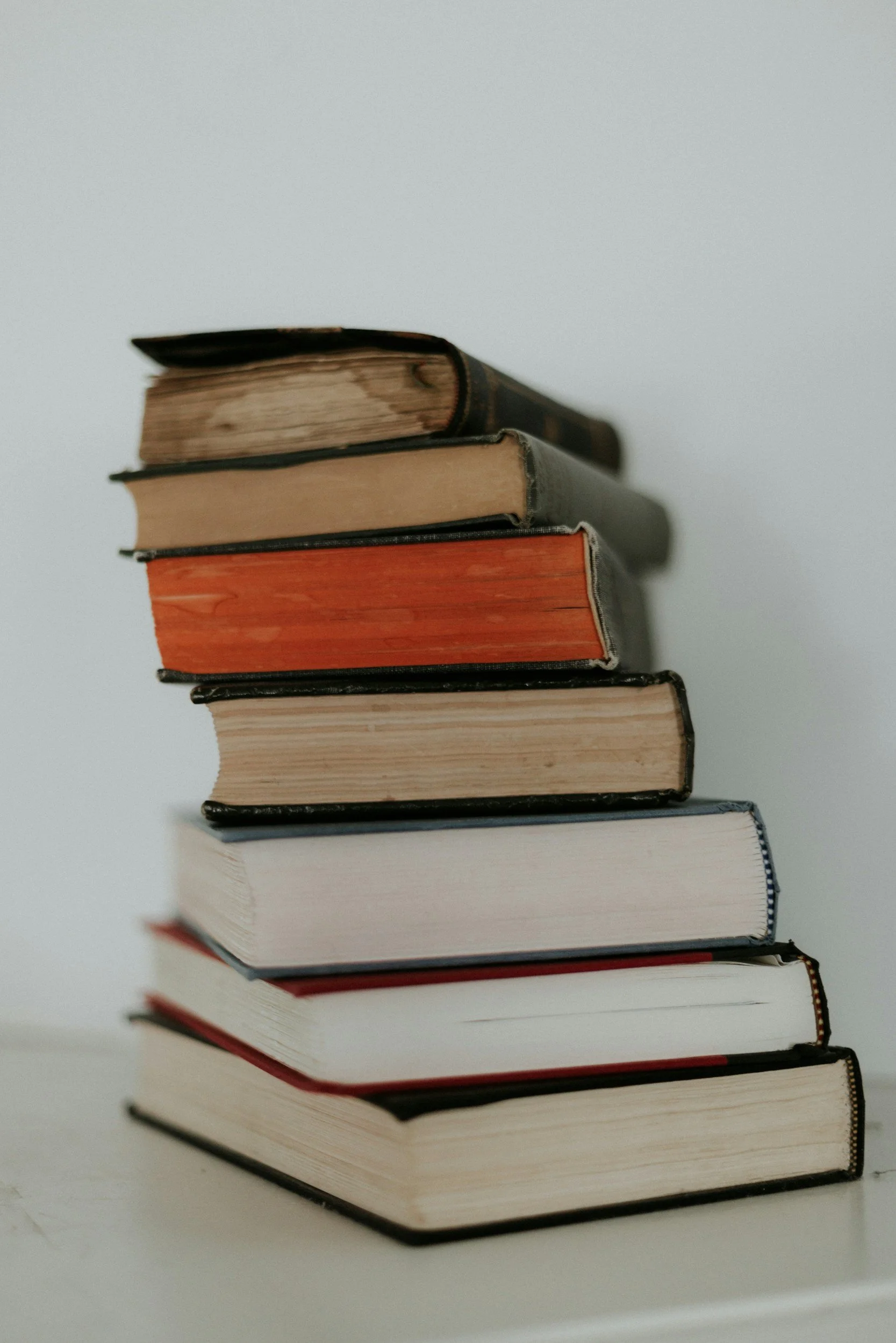 A stack of old and new books with worn covers and varying colors, placed on a white surface against a plain white background.